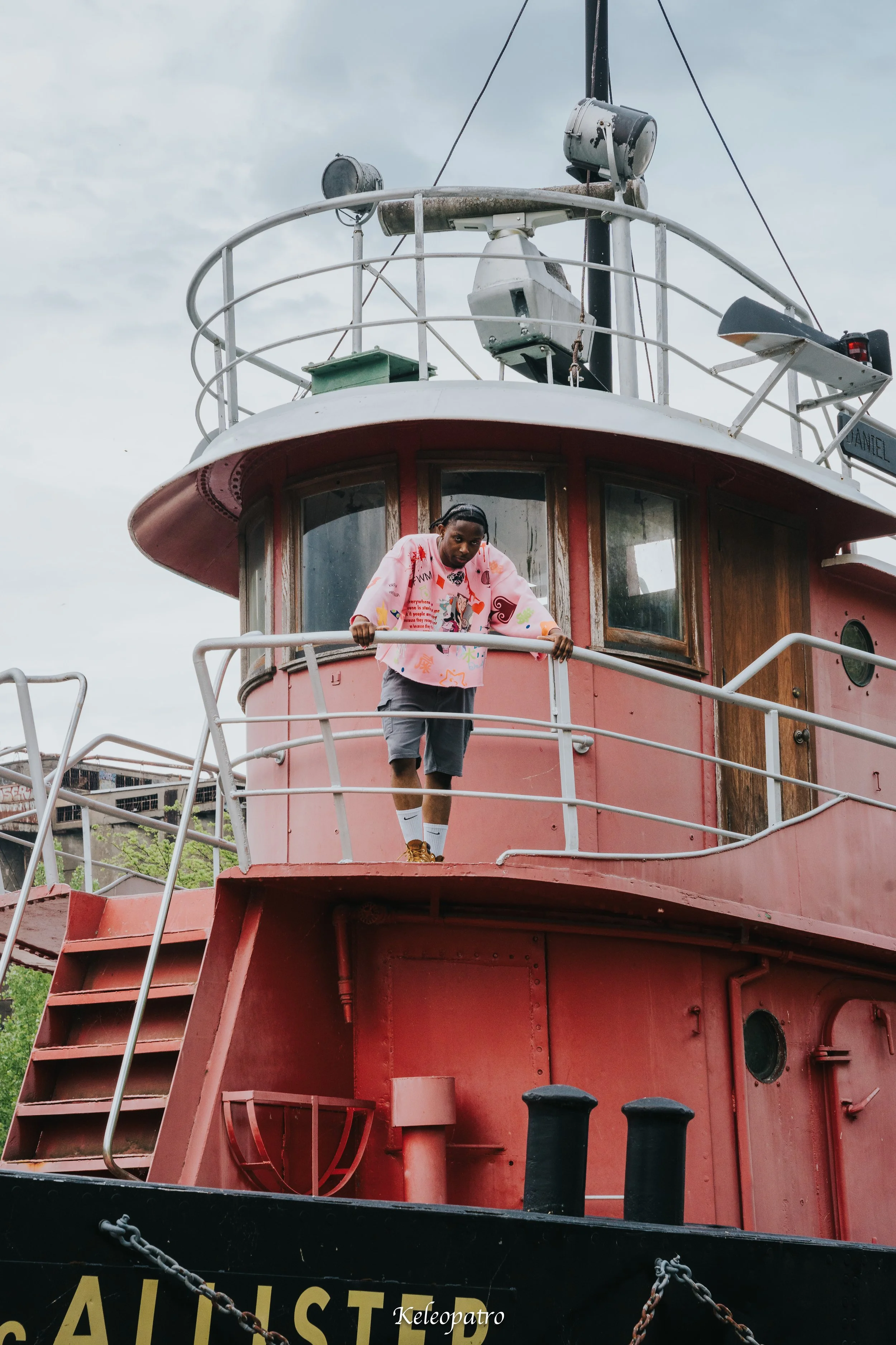 Une personne debout sur le pont d'un bateau rouge avec des fenêtres en bois, sous un ciel nuageux.