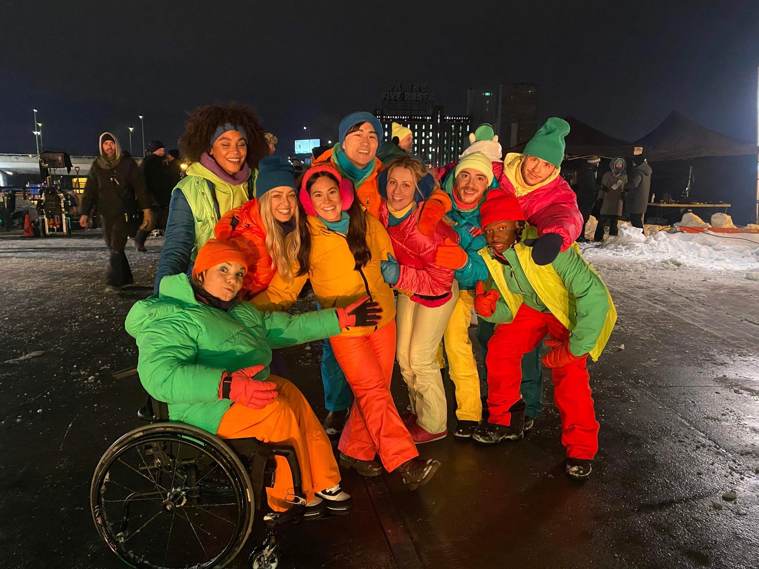Groupe de personnes souriantes en vêtements colorés d'hiver, posant ensemble dans un lieu enneigé la nuit.