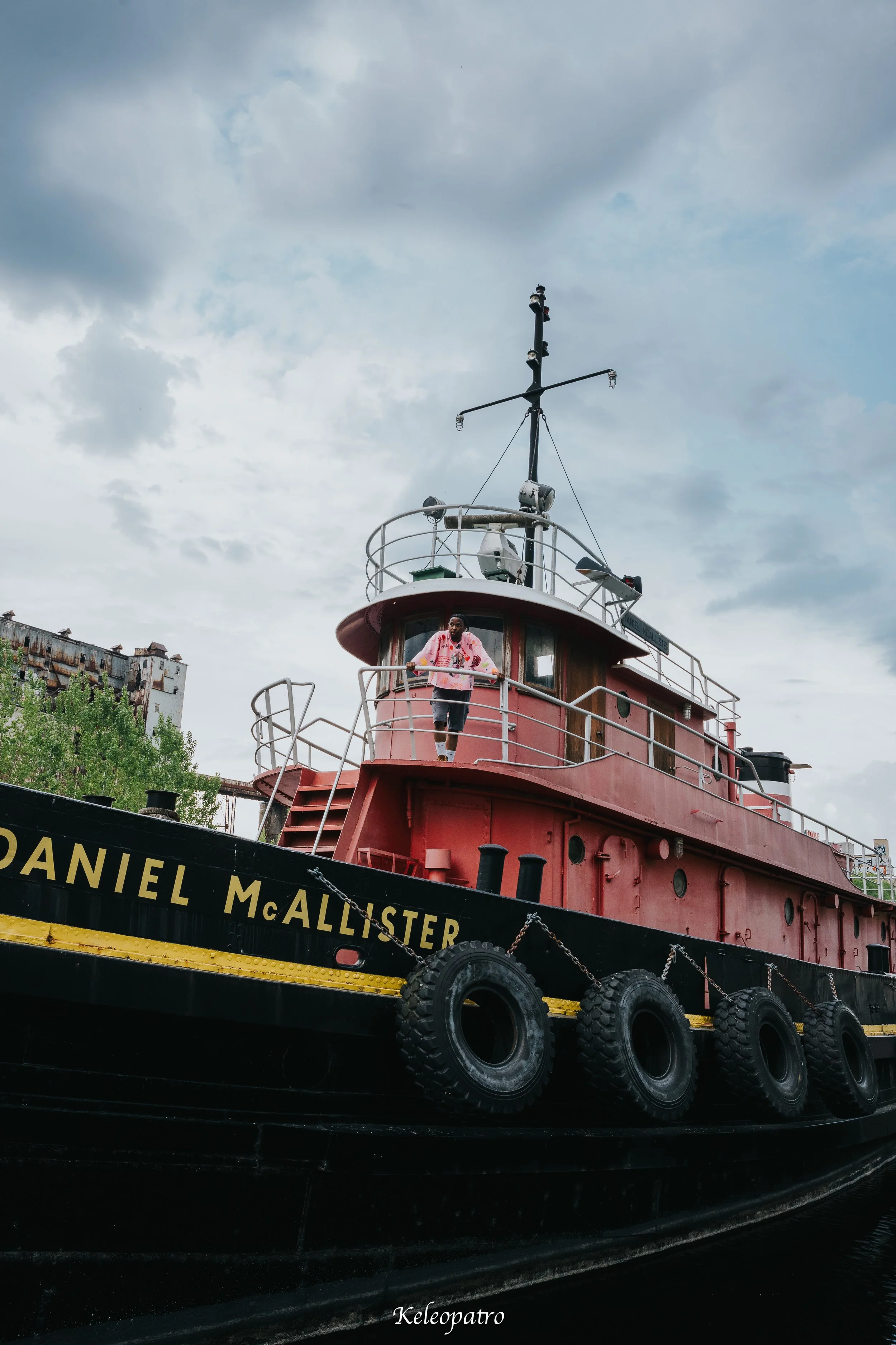 Un bateau nommé 'Daniel McAllister' avec une personne debout sur le pont supérieur, portant un sweat rose, sous un ciel nuageux.