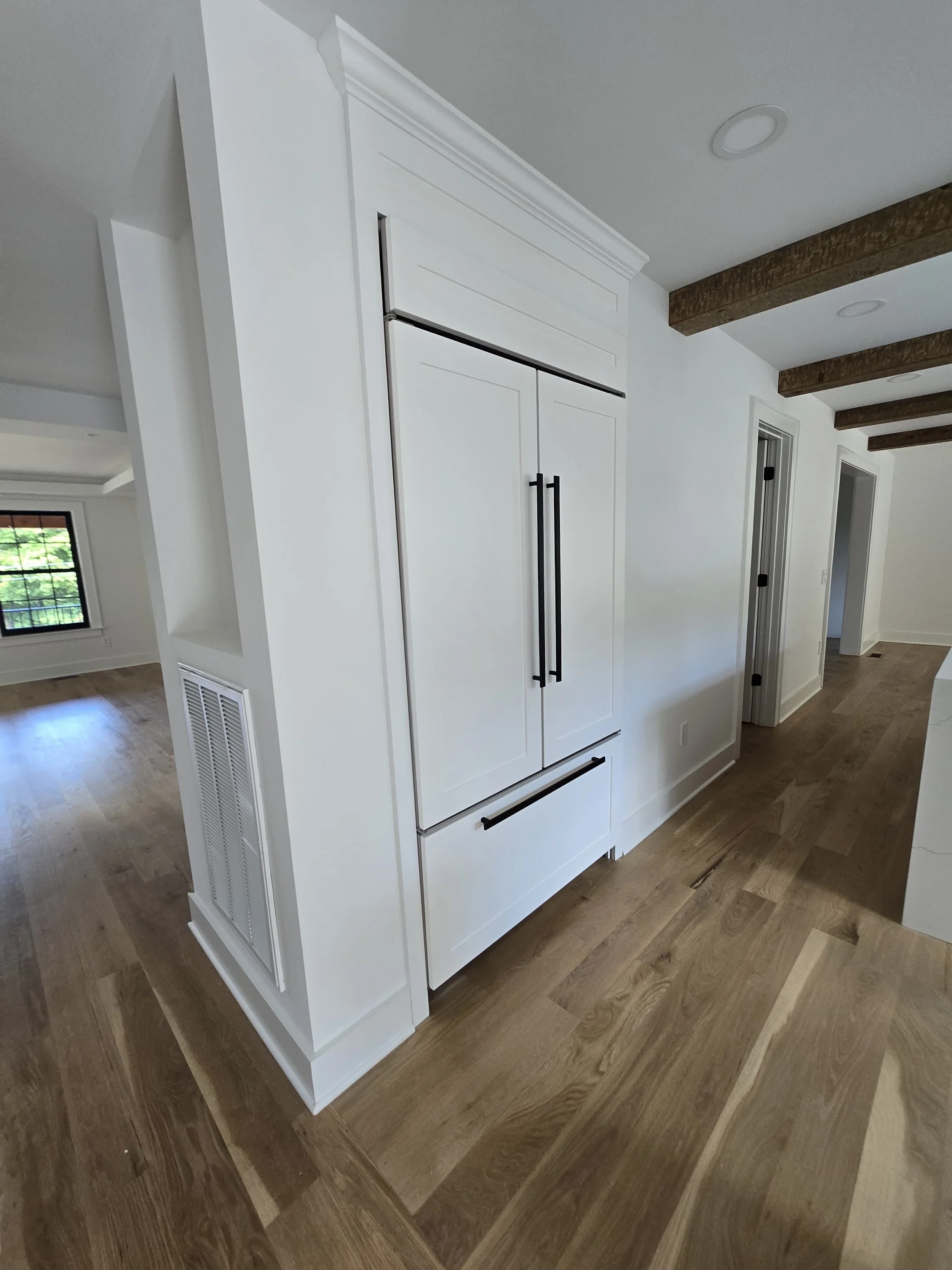 White kitchen cabinetry with black handles and wooden flooring in a modern home interior.