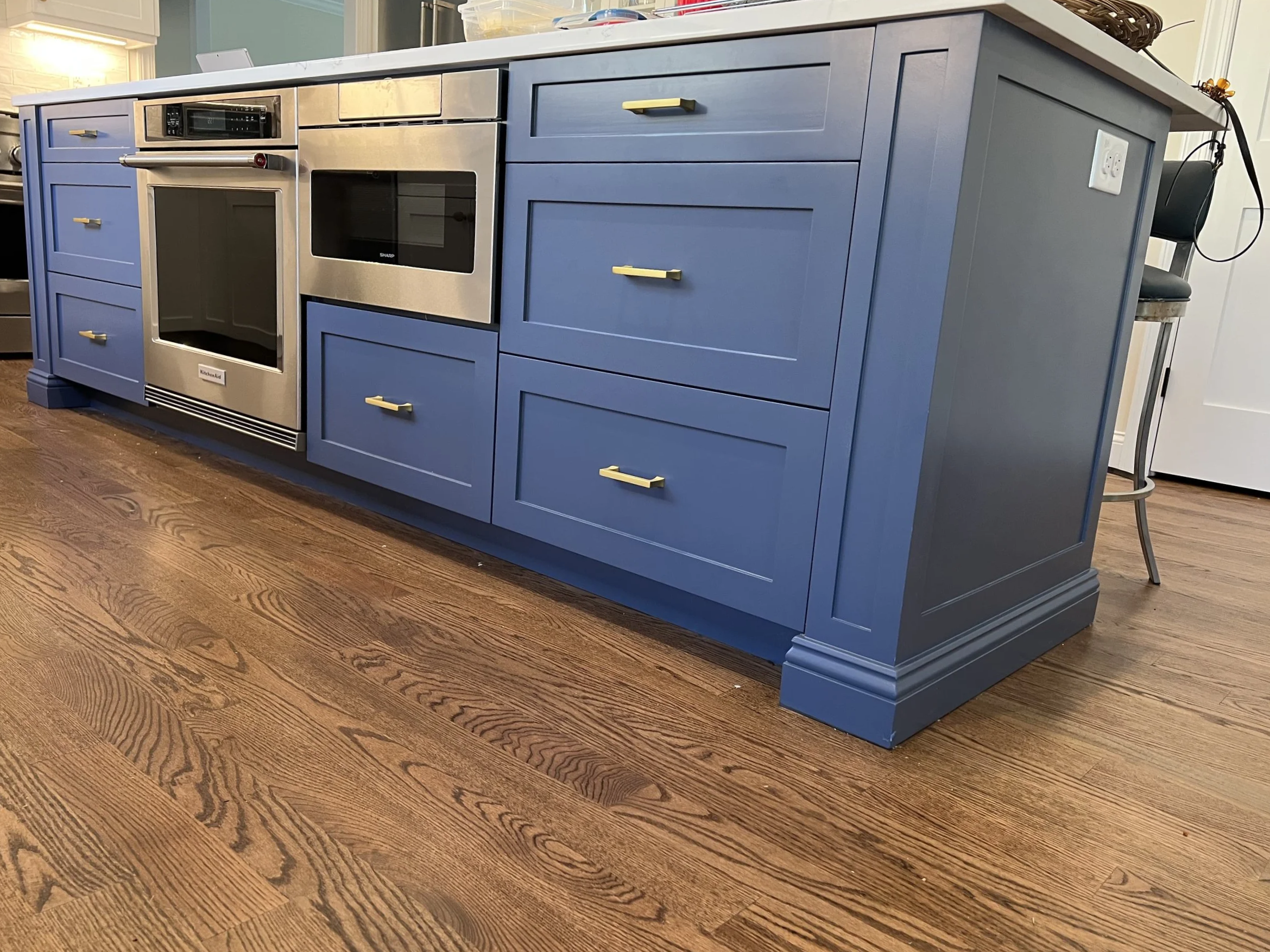 Blue kitchen island with drawers and cabinets, stainless steel oven and microwave, and hardwood flooring.
