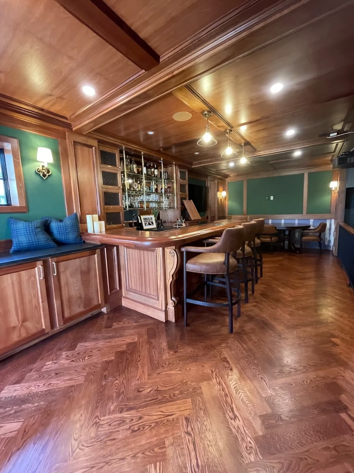 Elegant bar with wooden paneling, marble countertop, green walls, and subdued lighting, featuring bar stools and a back bar with liquor bottles.