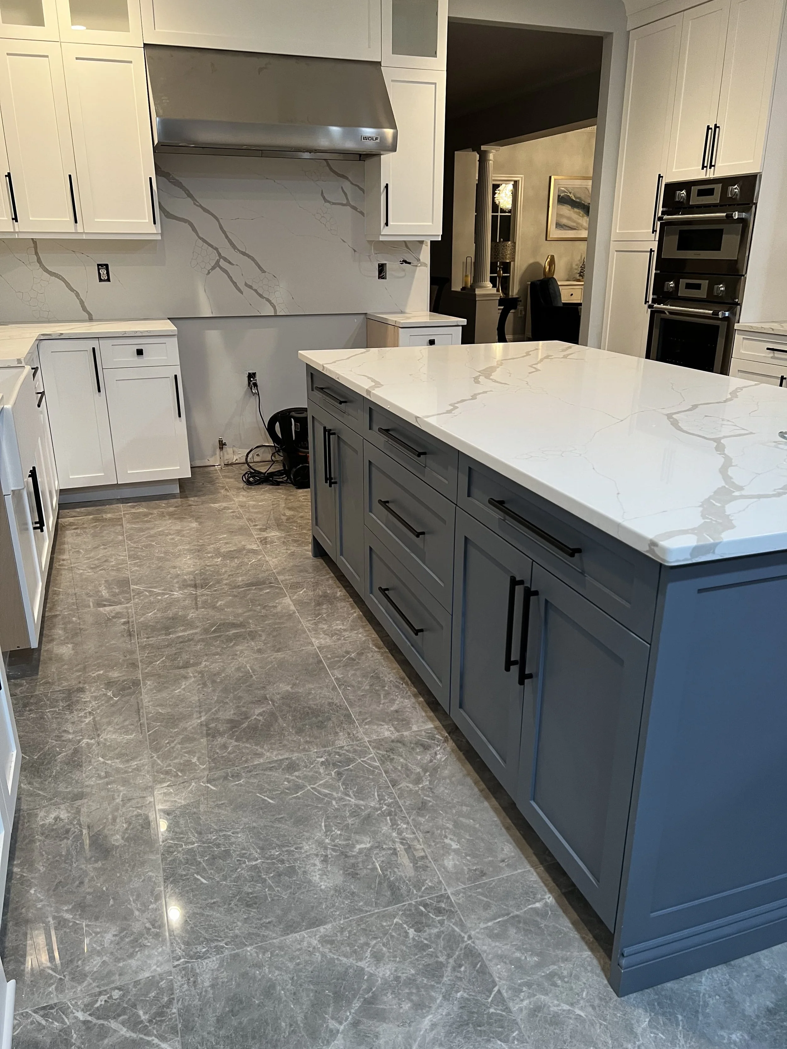 Modern kitchen with white and gray cabinetry, marble countertop island, gray marble floor, and stainless steel appliances.