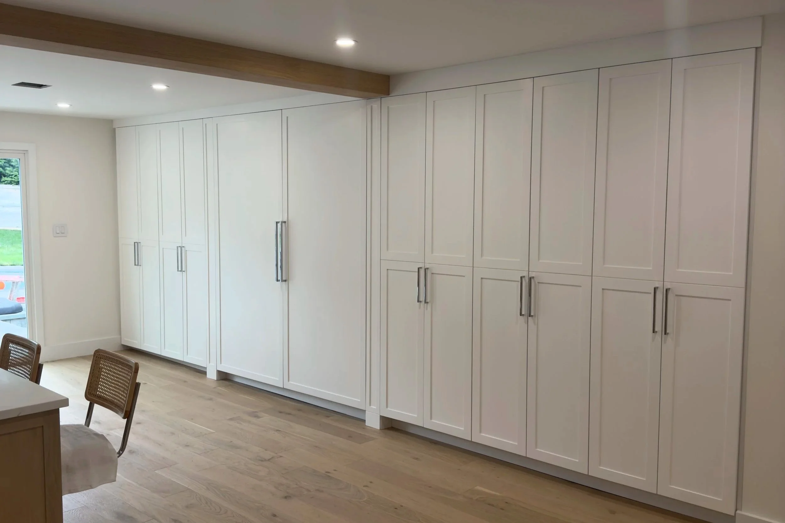 Modern kitchen with white cabinetry, wooden floor, and sliding glass door with outdoor view.