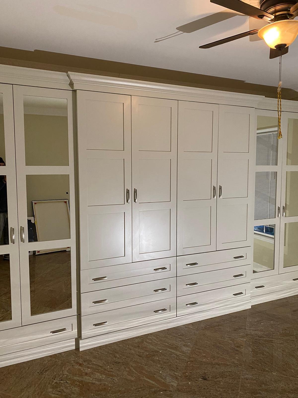 White built-in cabinet with glass doors and drawers in a room with brown flooring and ceiling fan with light