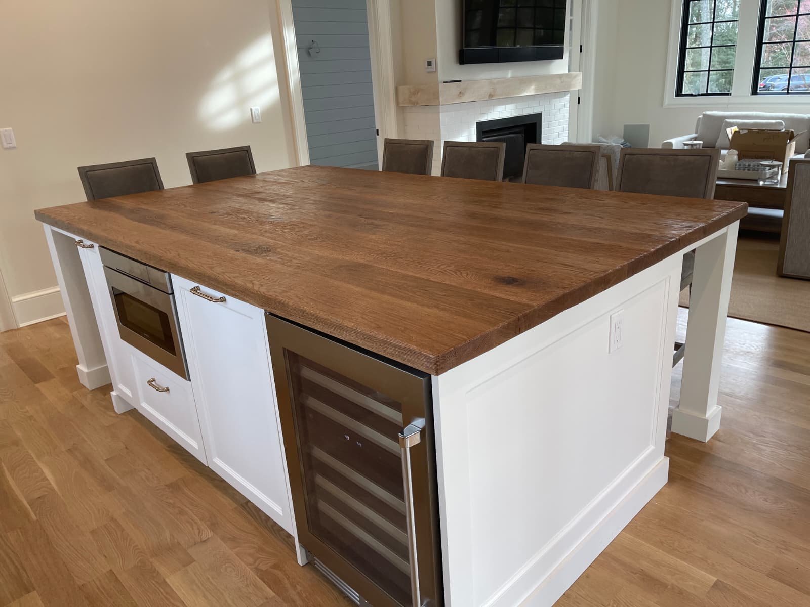 Kitchen island with a wooden top, built-in microwave, and small wine cooler, in a modern kitchen with hardwood floors and a dining area in the background.