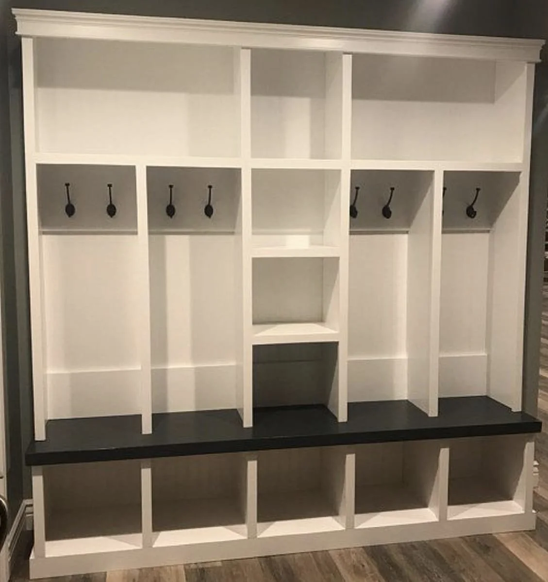 White and black wooden entryway organizer with hooks, cubbies, and shelves for coats and accessories.