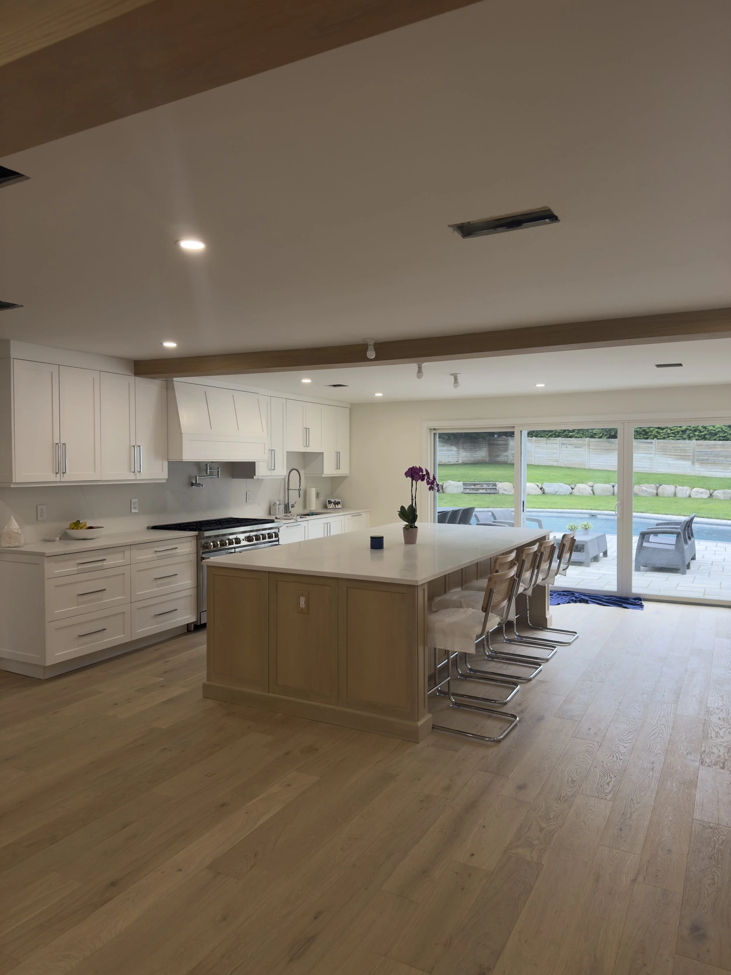 Modern kitchen with white cabinets, a large island with barstools, and sliding glass doors leading to an outdoor patio with lawn and seating area.