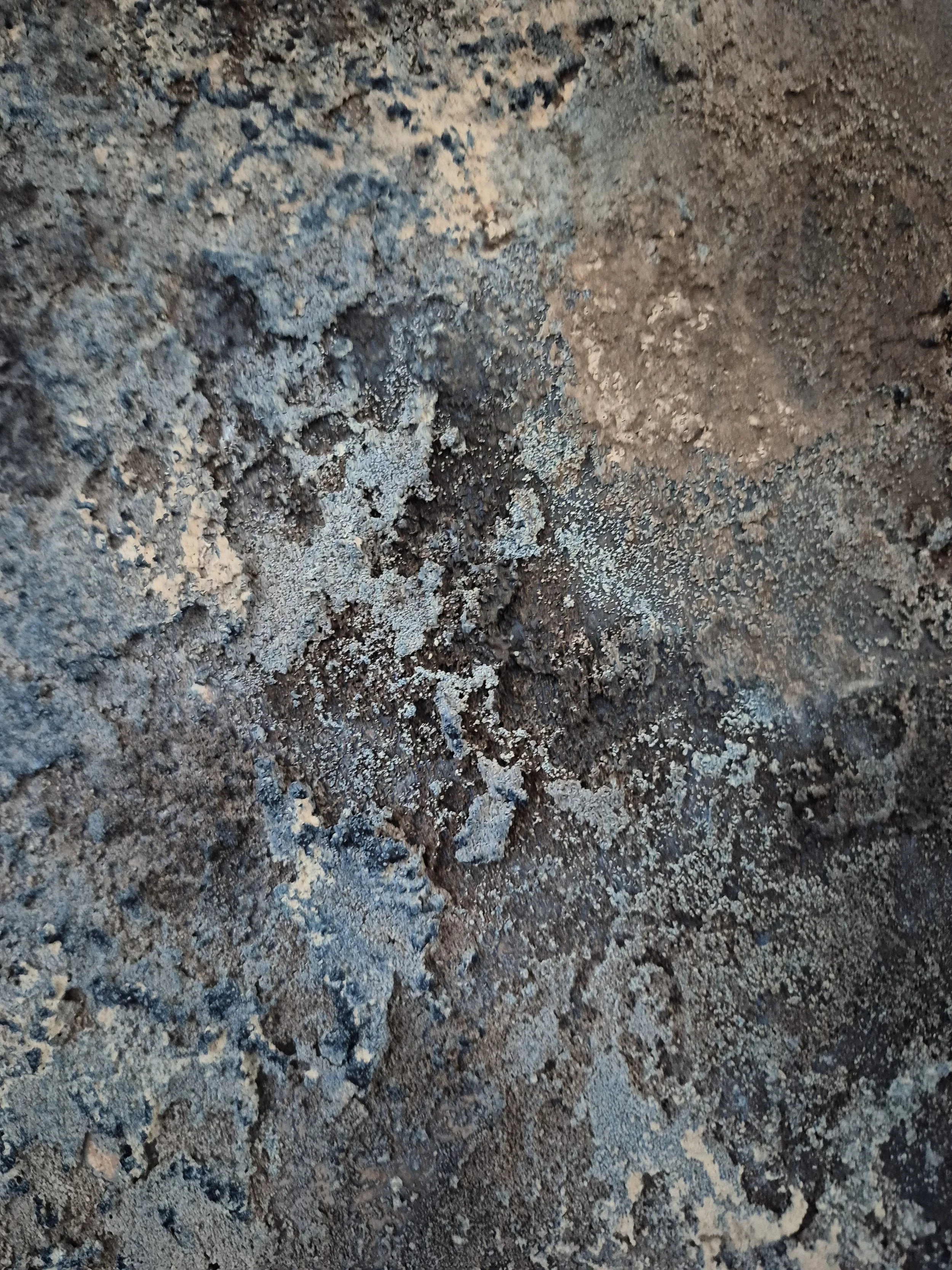 Rundt abstrakt maleri med kraftig tekstur i blå, grå og sorte nuancer, der minder om en planet eller en måneoverflade på en hvid baggrund.