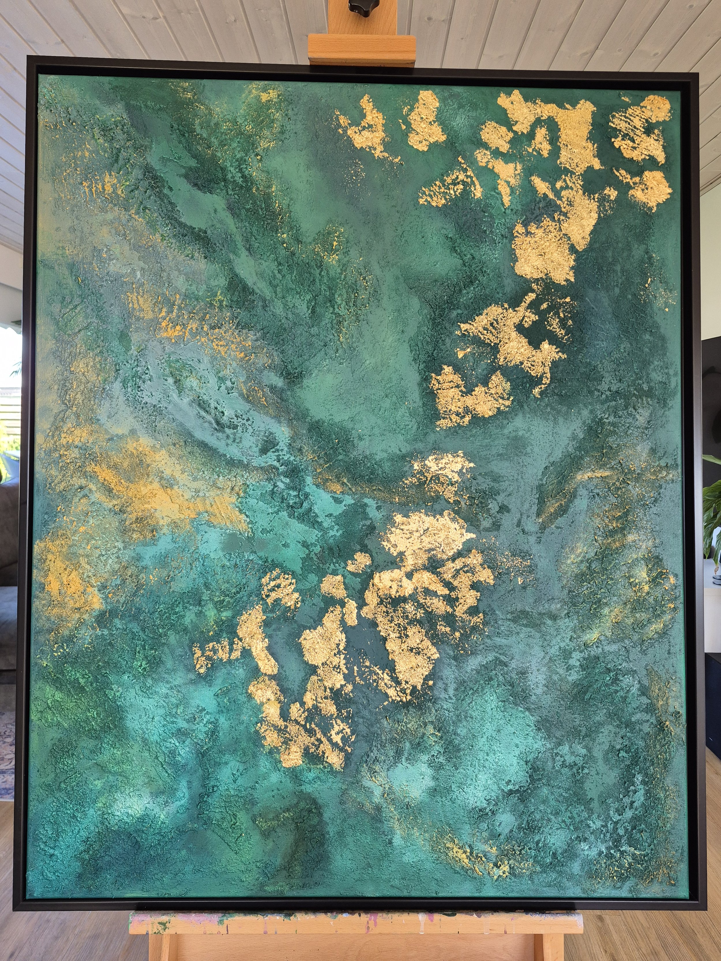 Abstrakt strukturmaleri i grønne og gyldne nuancer, skabt med en blanding af sand og akrylmaling for en grov, taktil overflade.
