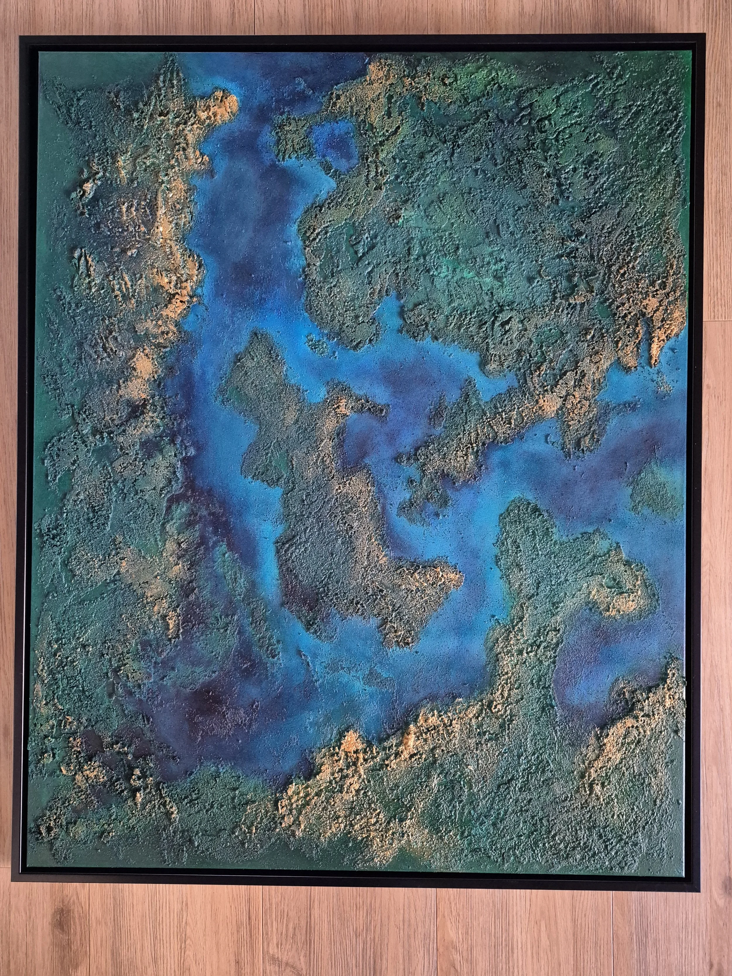 Stort 80x100 cm abstrakt maleri med kraftig tekstur af ægte strandsand. Motivet er i dybe blå, grønne og gyldne nuancer, der ligner et kystlandskab set fra oven.