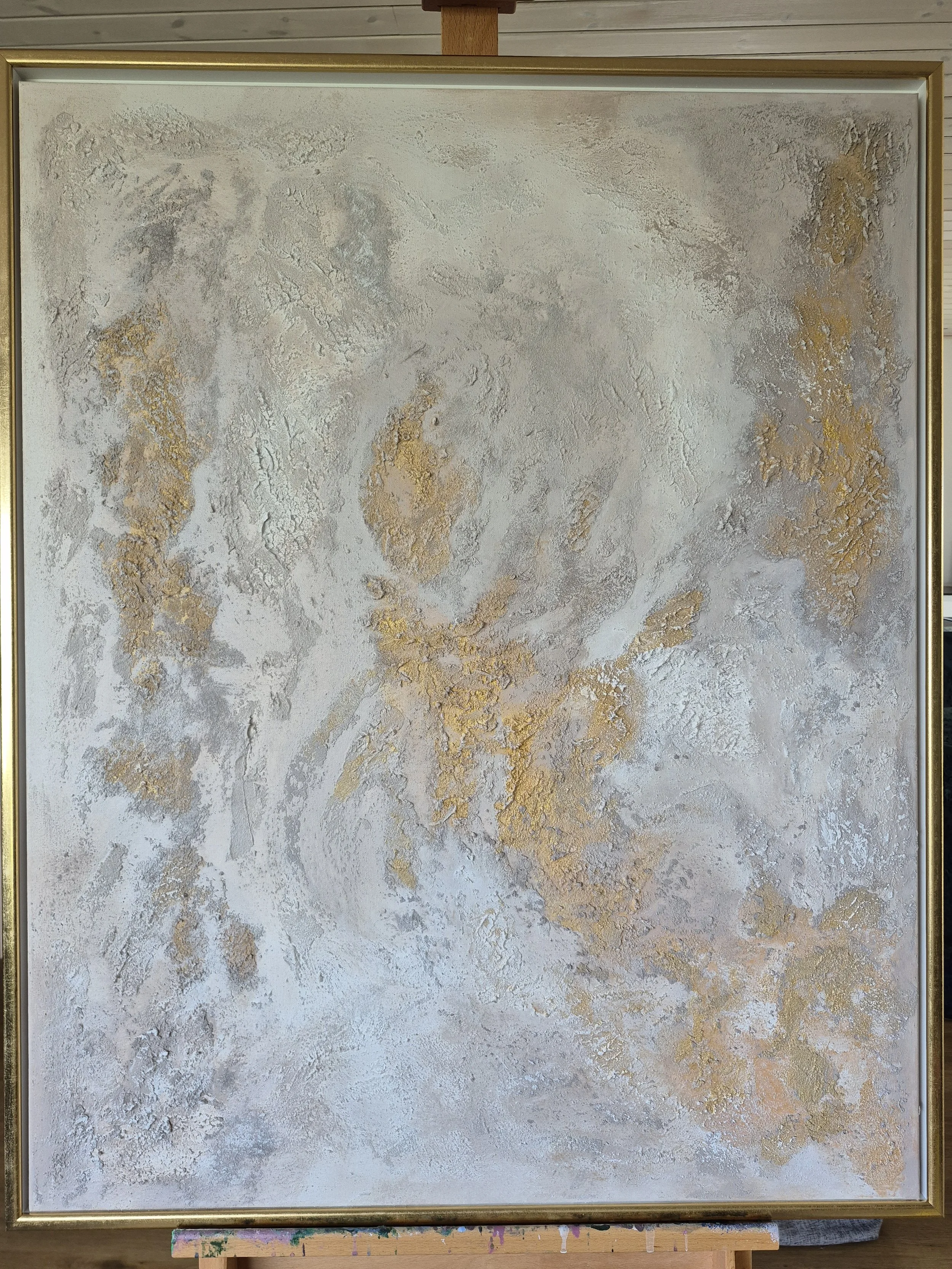 Abstrakt maleri i hvide og guld nuancer (80x100 cm) placeret i en lys, skandinavisk stue med store planter.