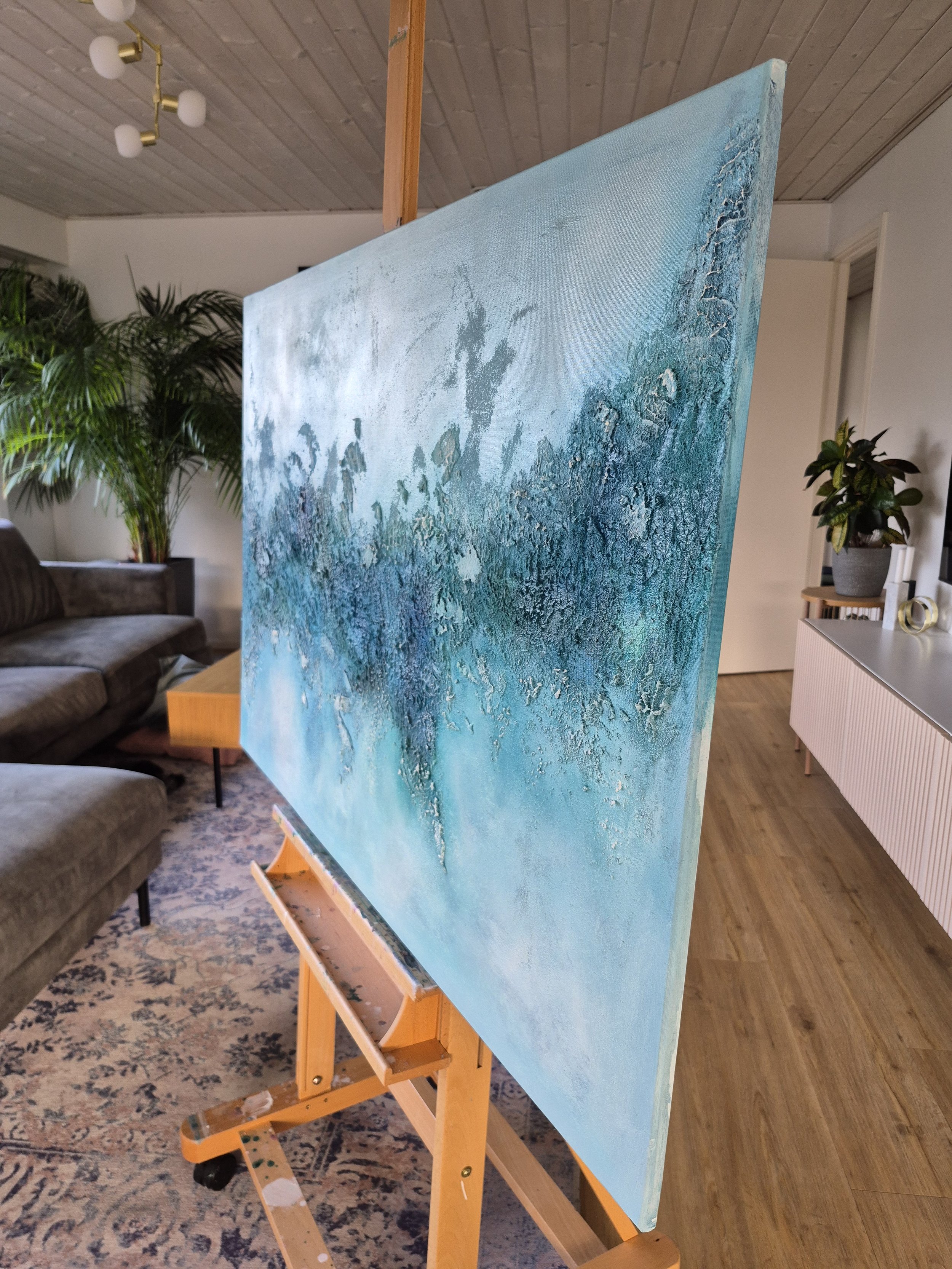 Stort blåt og turkist abstrakt maleri med titlen Continuum hængt op over en grå sofa i en moderne stue.