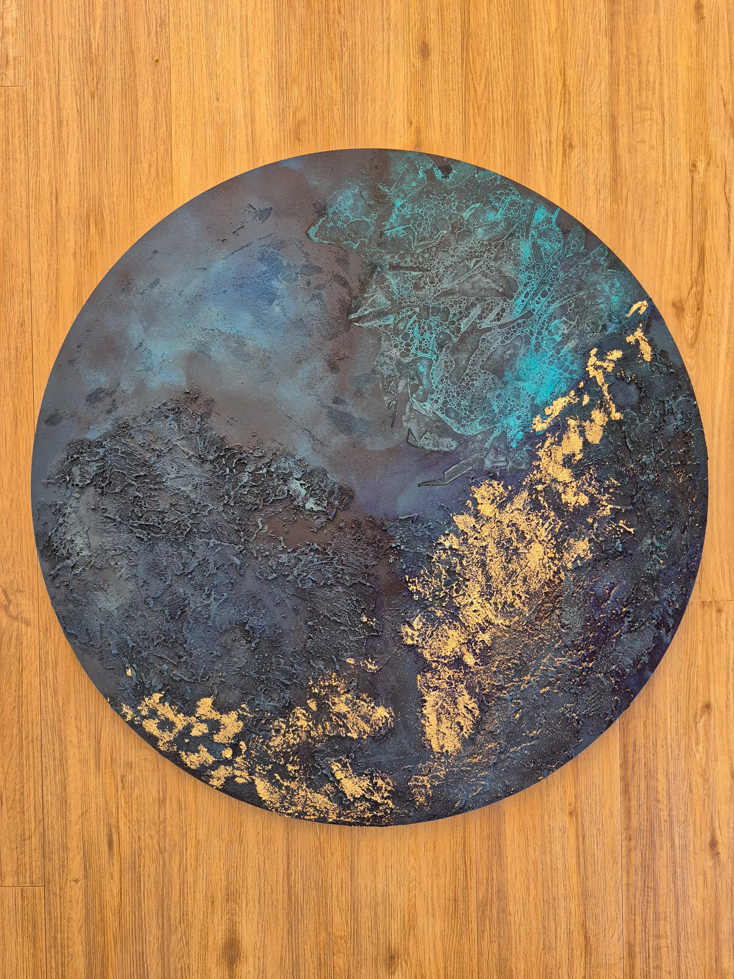 ​Modern living room featuring a large circular abstract wall art piece with deep teal, navy, and gold leaf textures.