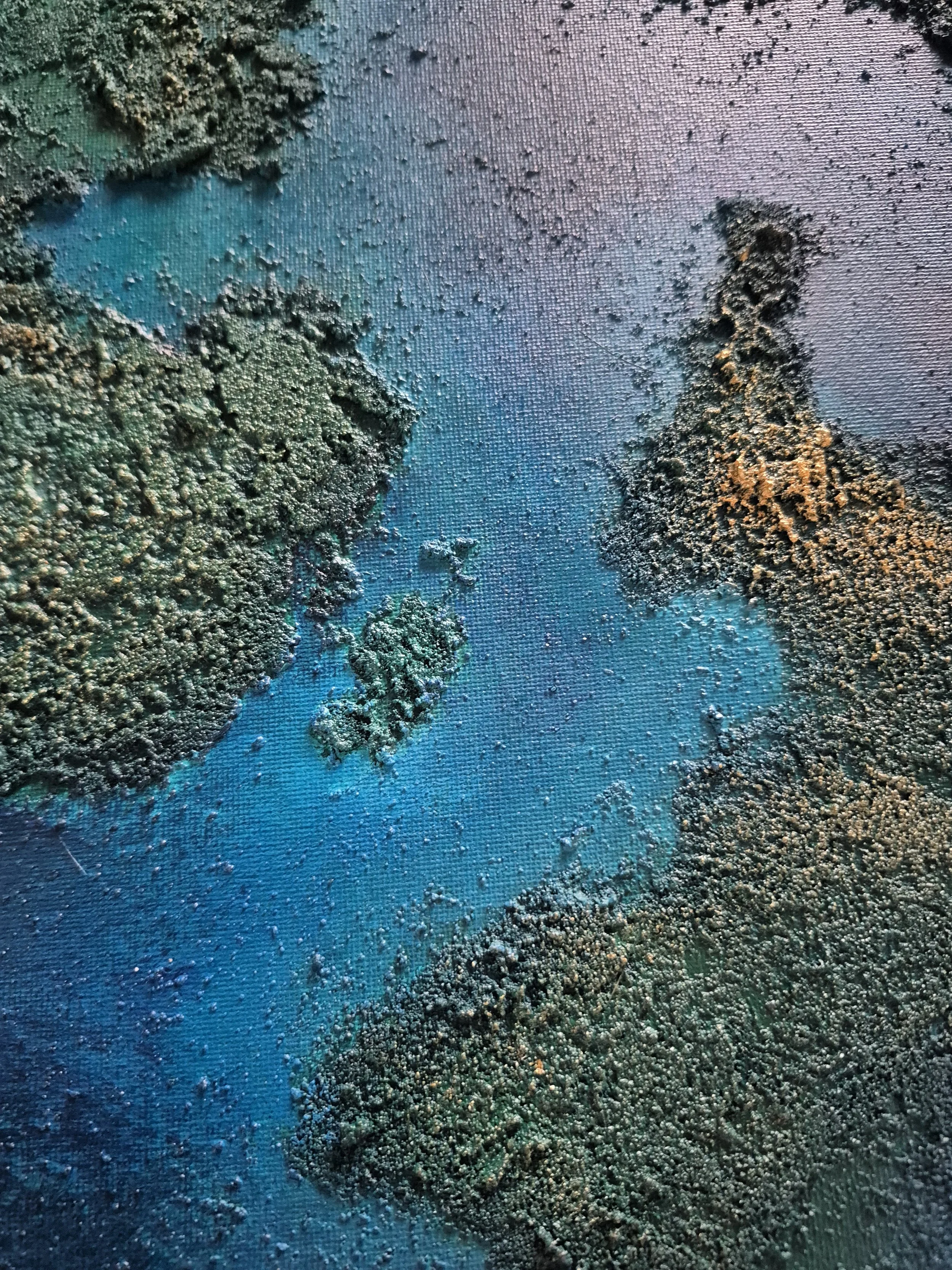 Stort 80x100 cm abstrakt maleri med kraftig tekstur af ægte strandsand. Motivet er i dybe blå, grønne og gyldne nuancer, der ligner et kystlandskab set fra oven.