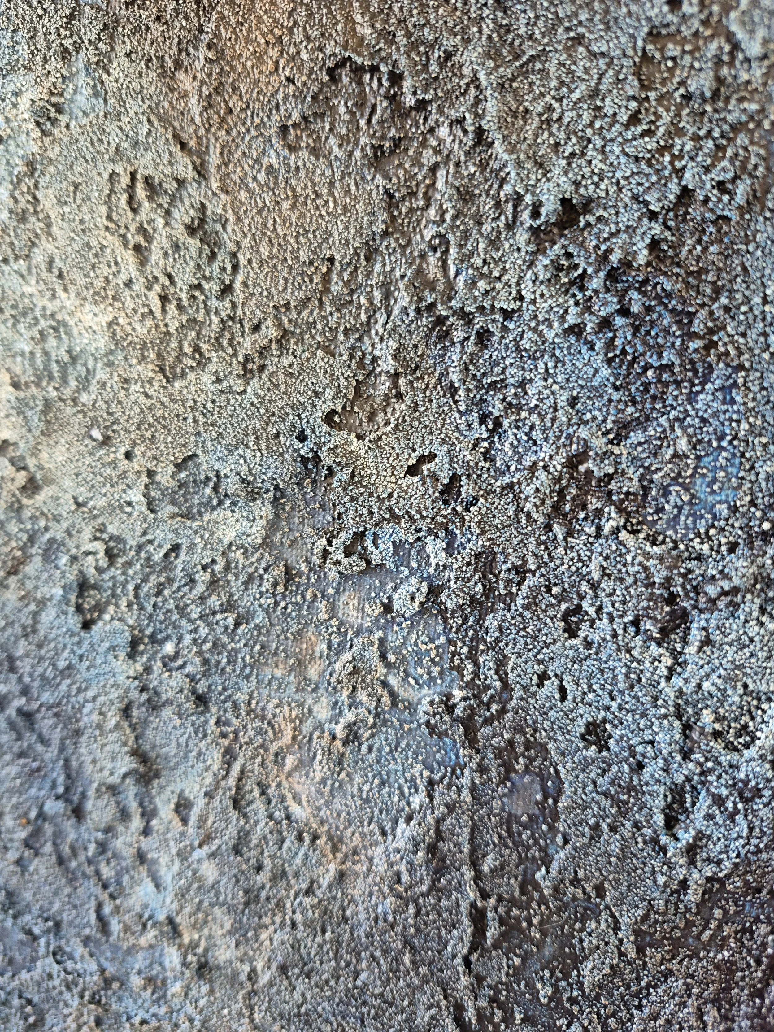 Stort abstrakt maleri med titlen 'Cosmos' udstillet på et staffeli. Maleriet har en kraftig struktur af sand og akryl i blå, grå og beige nuancer, indrammet i en lys træramme.