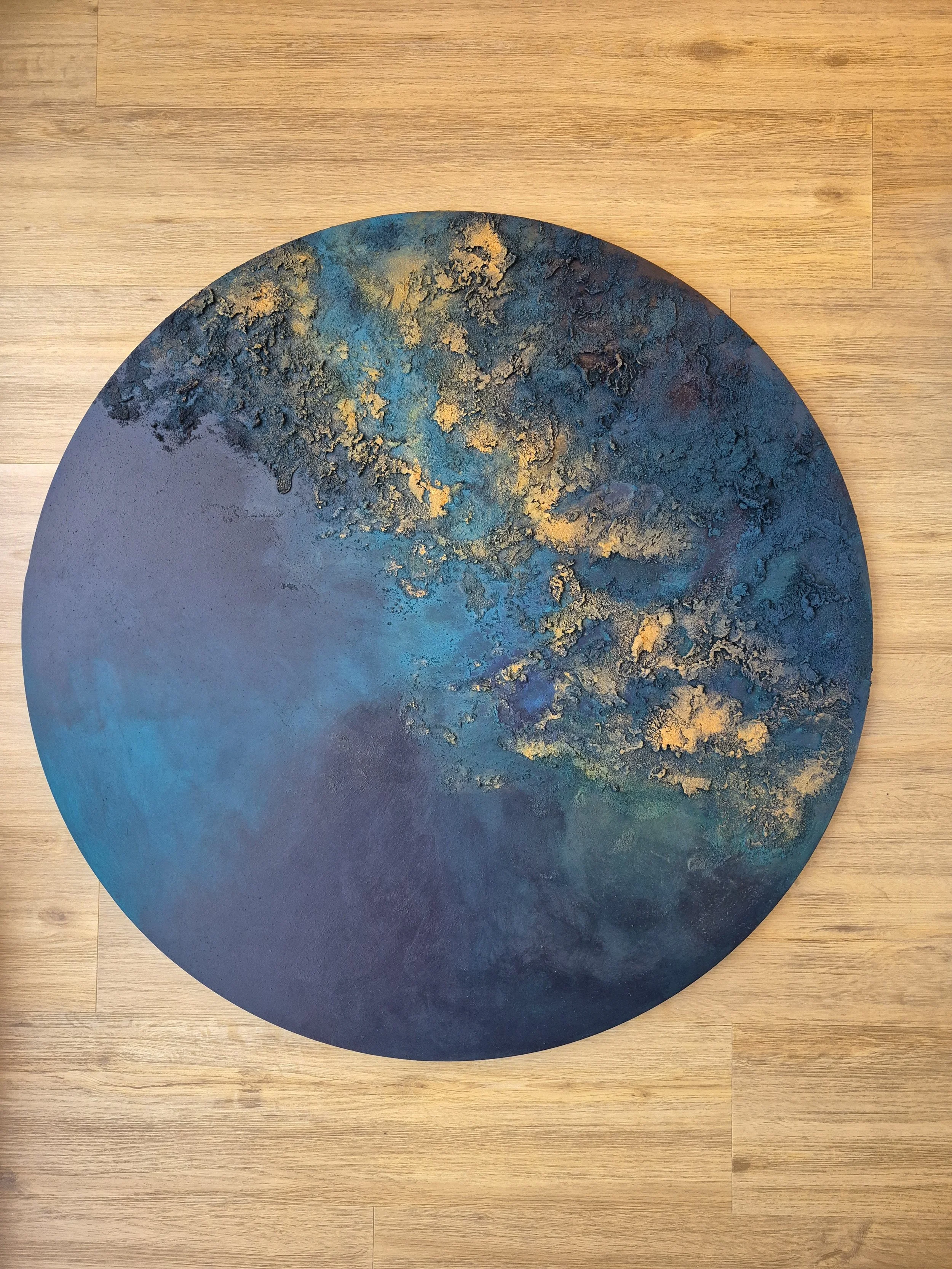 Large 1-meter circular abstract painting featuring deep indigo and navy blue textures with raised metallic gold leaf accents, styled in a modern Scandinavian bedroom.