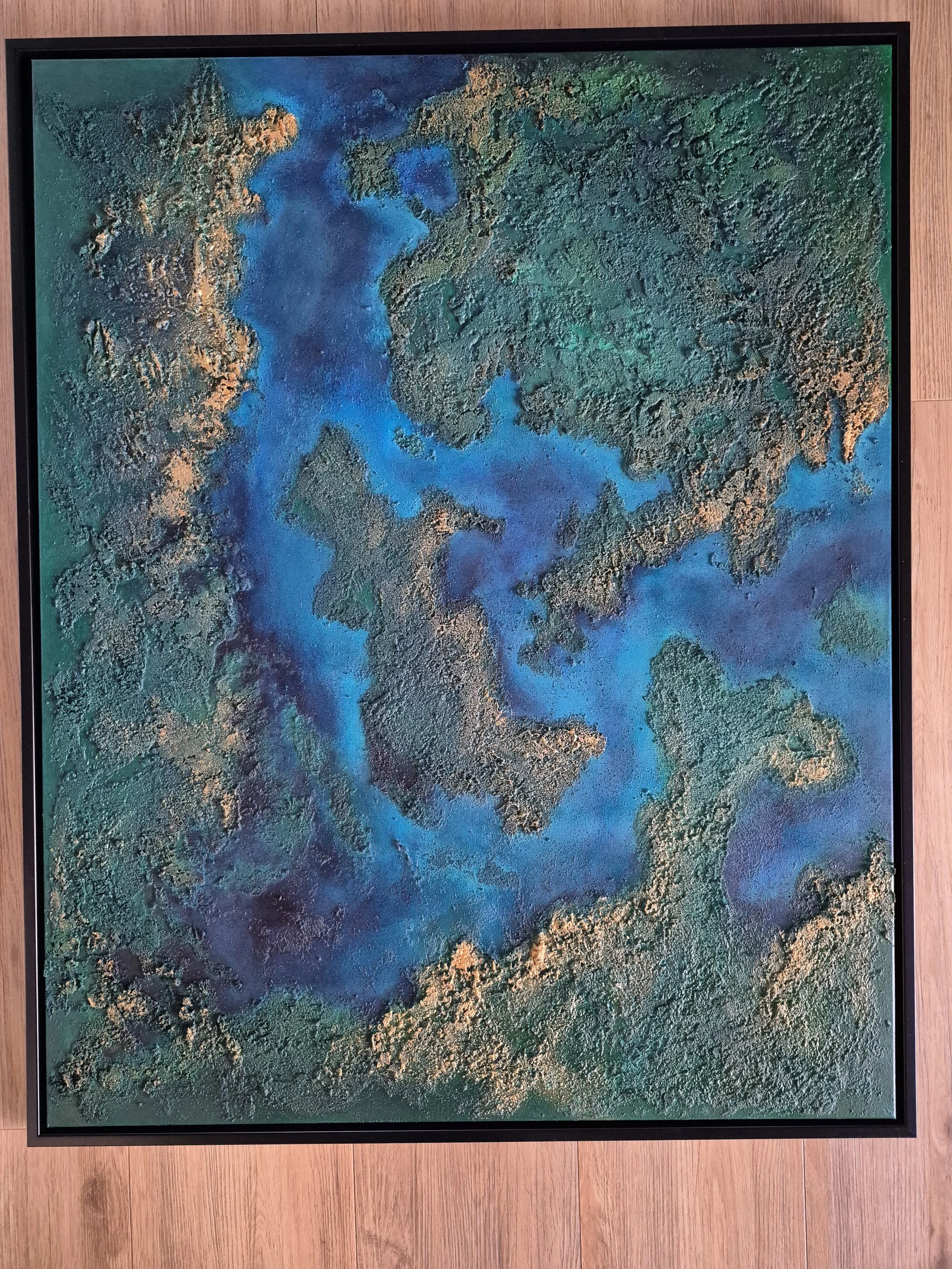 Stort 80x100 cm abstrakt maleri med kraftig tekstur af ægte strandsand. Motivet er i dybe blå, grønne og gyldne nuancer, der ligner et kystlandskab set fra oven.