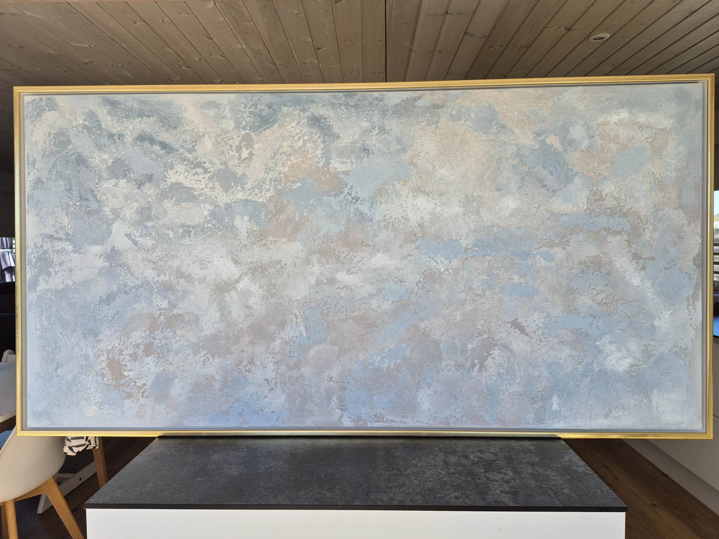 Stort abstrakt maleri med titlen Ethereal i blålige og grålige nuancer, 80x160 cm, monteret i guldramme i en moderne stue.