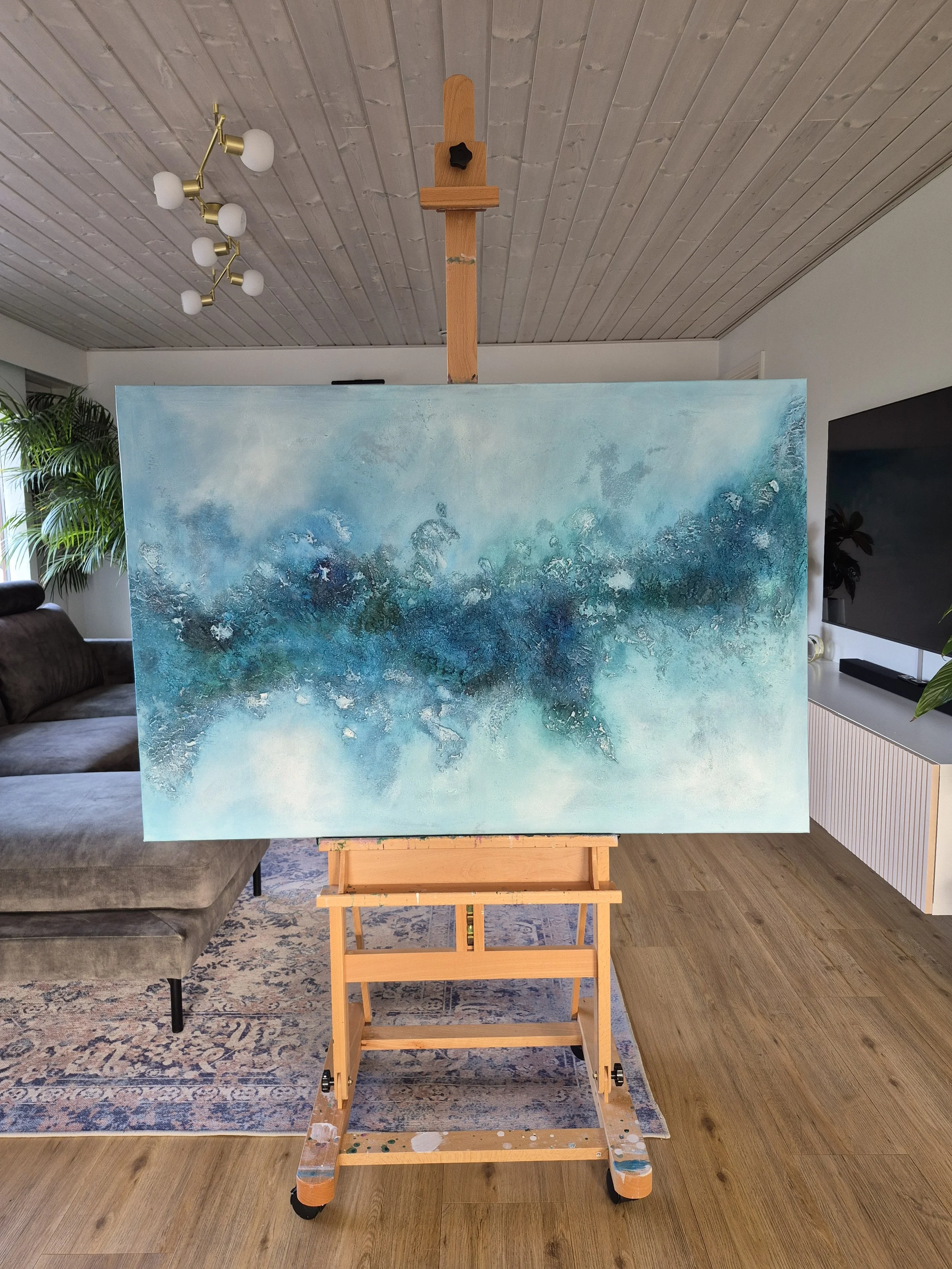 Stort blåt og turkist abstrakt maleri med titlen Continuum hængt op over en grå sofa i en moderne stue.