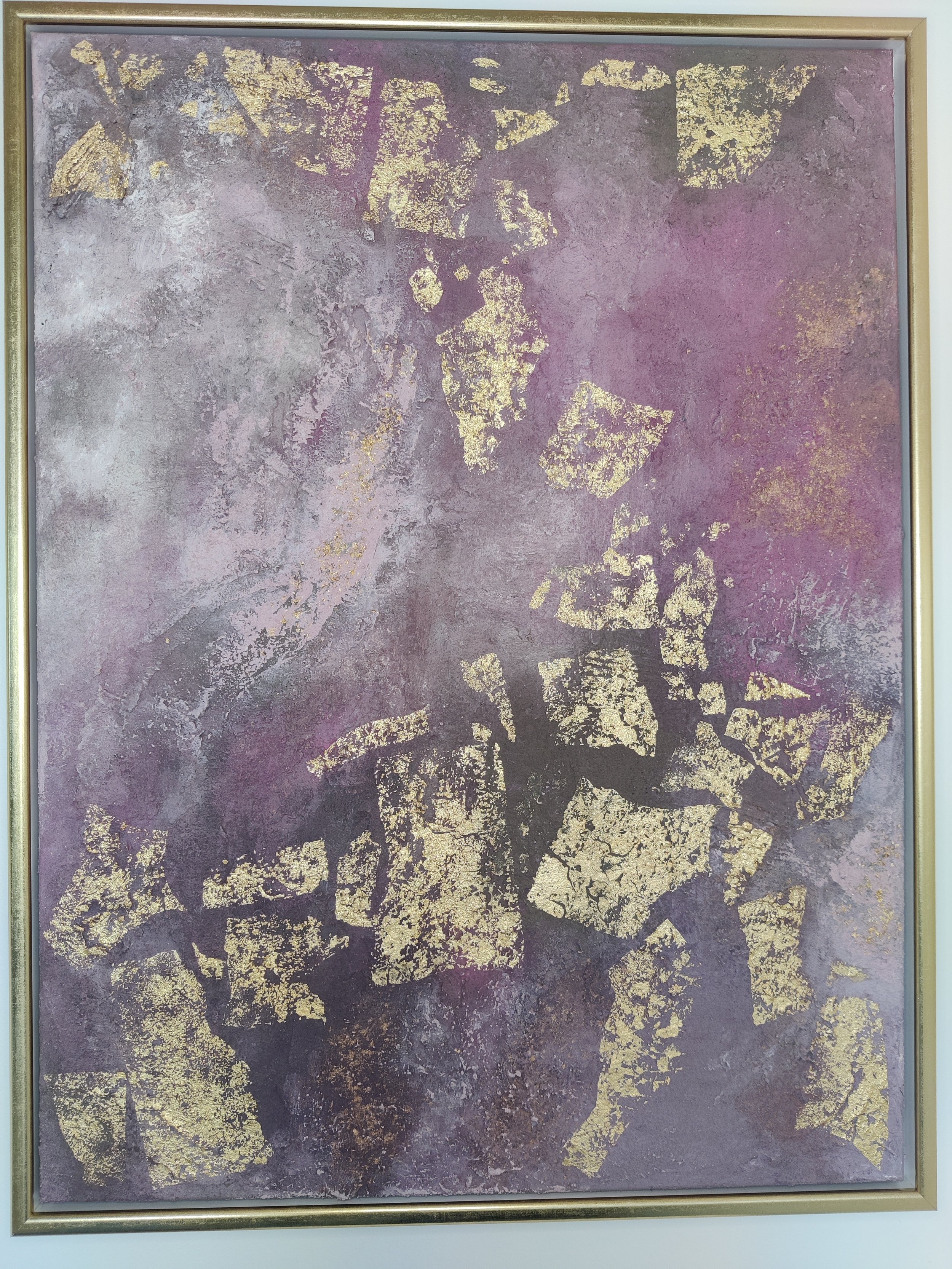 Abstrakt maleri i lilla og rosa nuancer med grov sandstruktur og store guldflager i en smal guldramme.