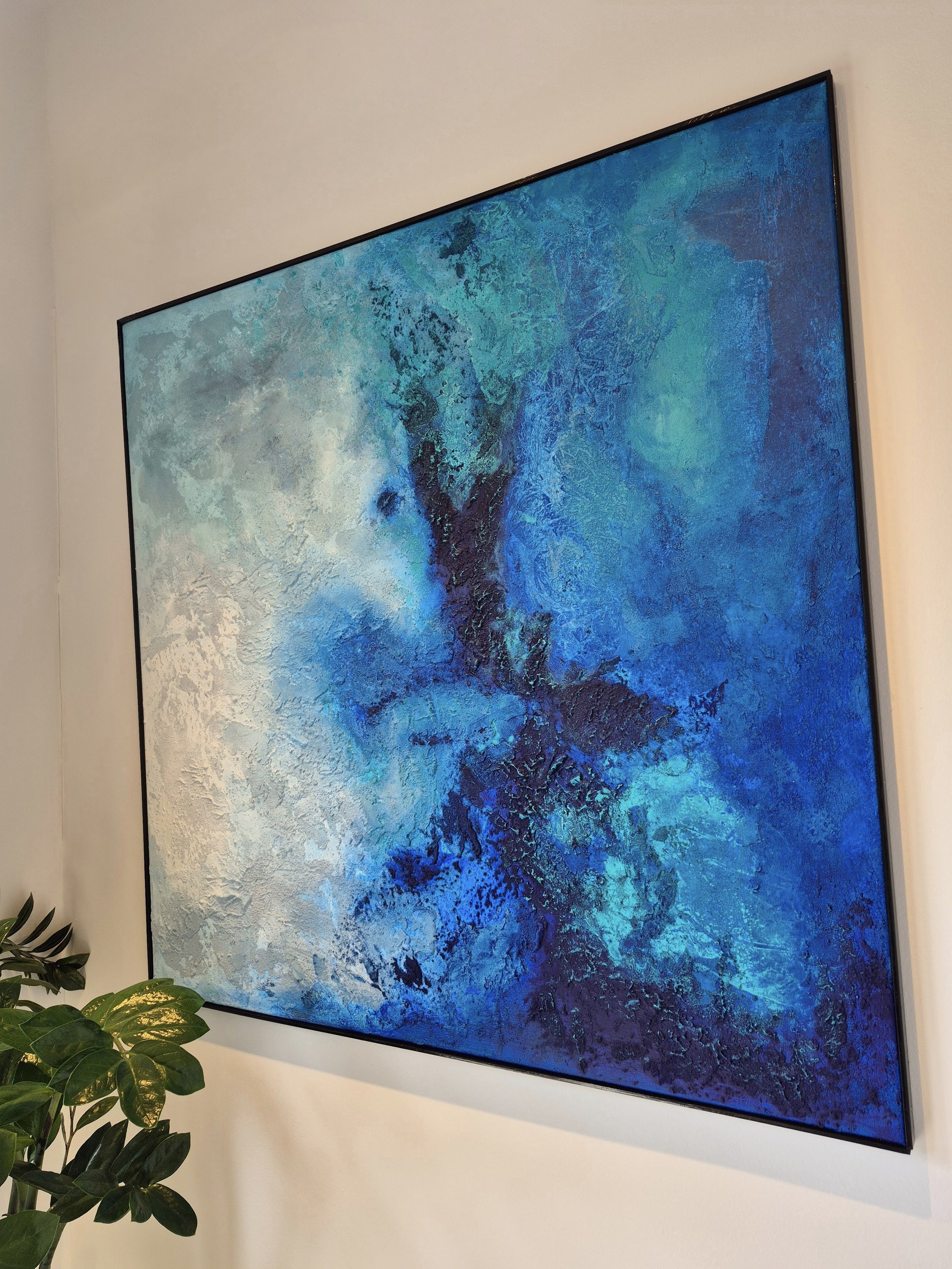 Stort kvadratisk abstrakt akrylmaleri på 100x100 cm i en sort ramme. Værket viser en tekstureret overflade med nordisk sandstruktur i nuancer af mørkeblå, turkis og hvide lysglimt