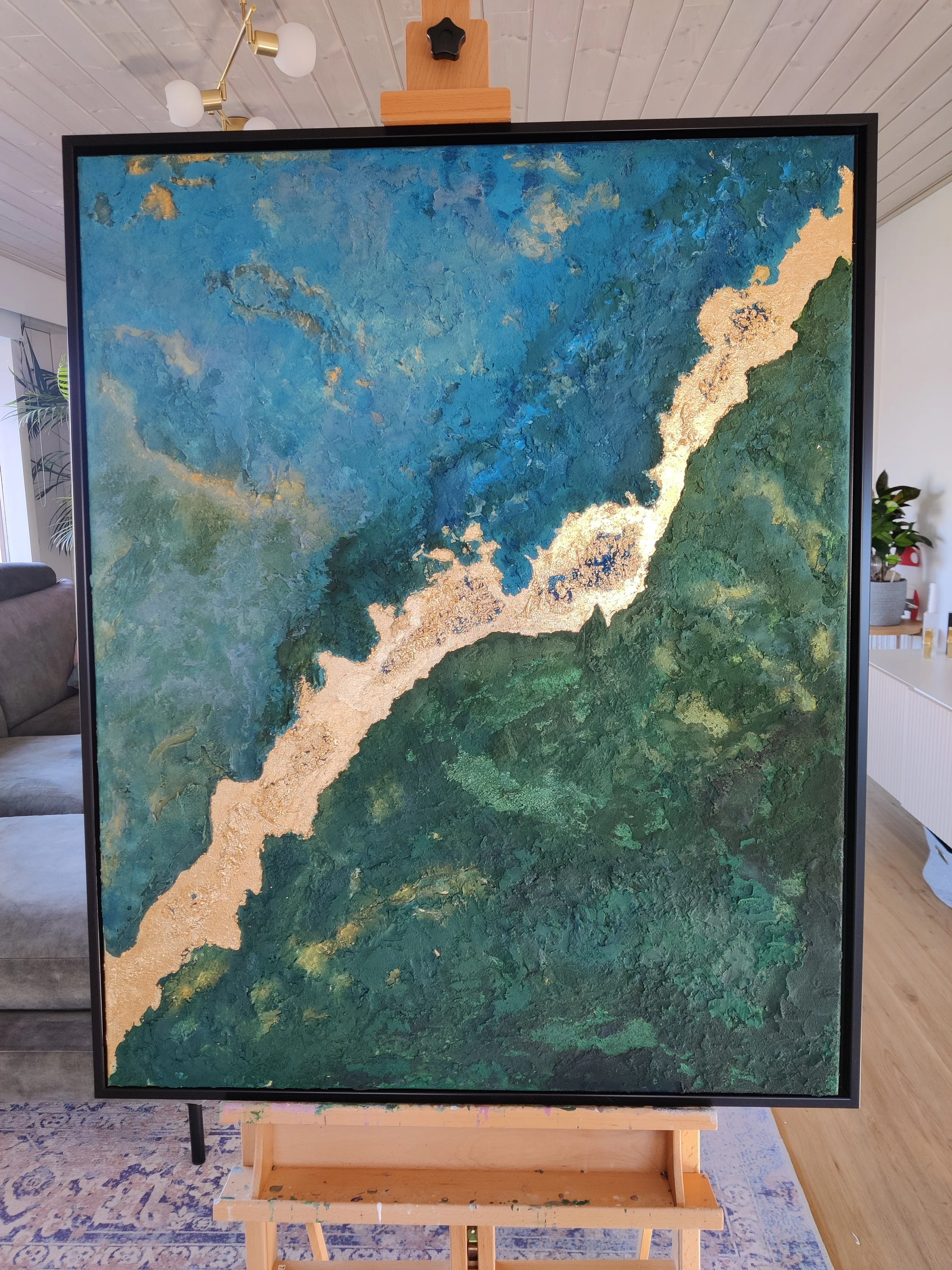 Stort abstrakt maleri 80x100 cm i skandinavisk stue med blå, grønne og guld nuancer monteret i sort svæveramme.