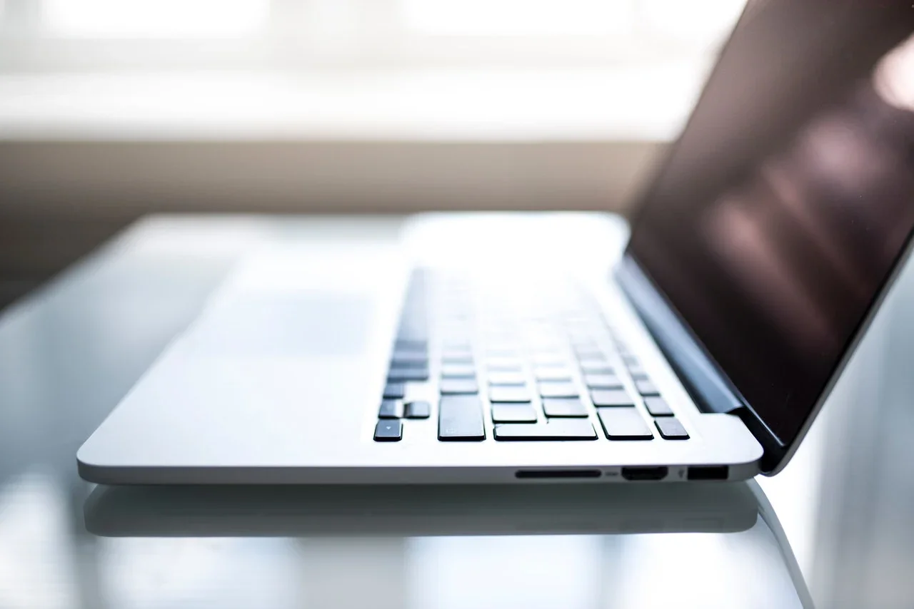Close-up of a silver laptop computer with black keys on a white surface, illuminated by natural light.