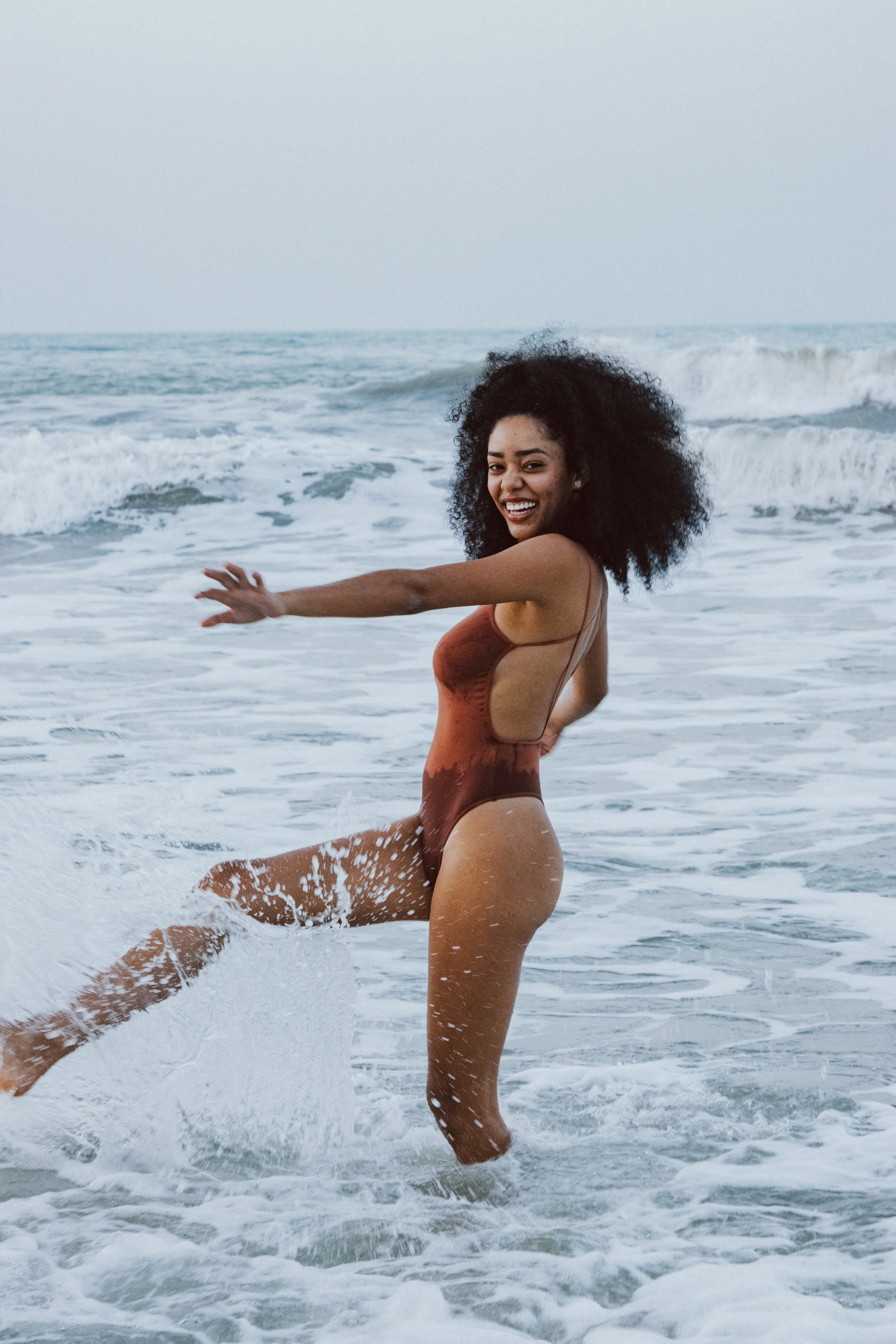 A woman happily playing in the ocean waves at the beach, wearing a one-piece swimsuit.