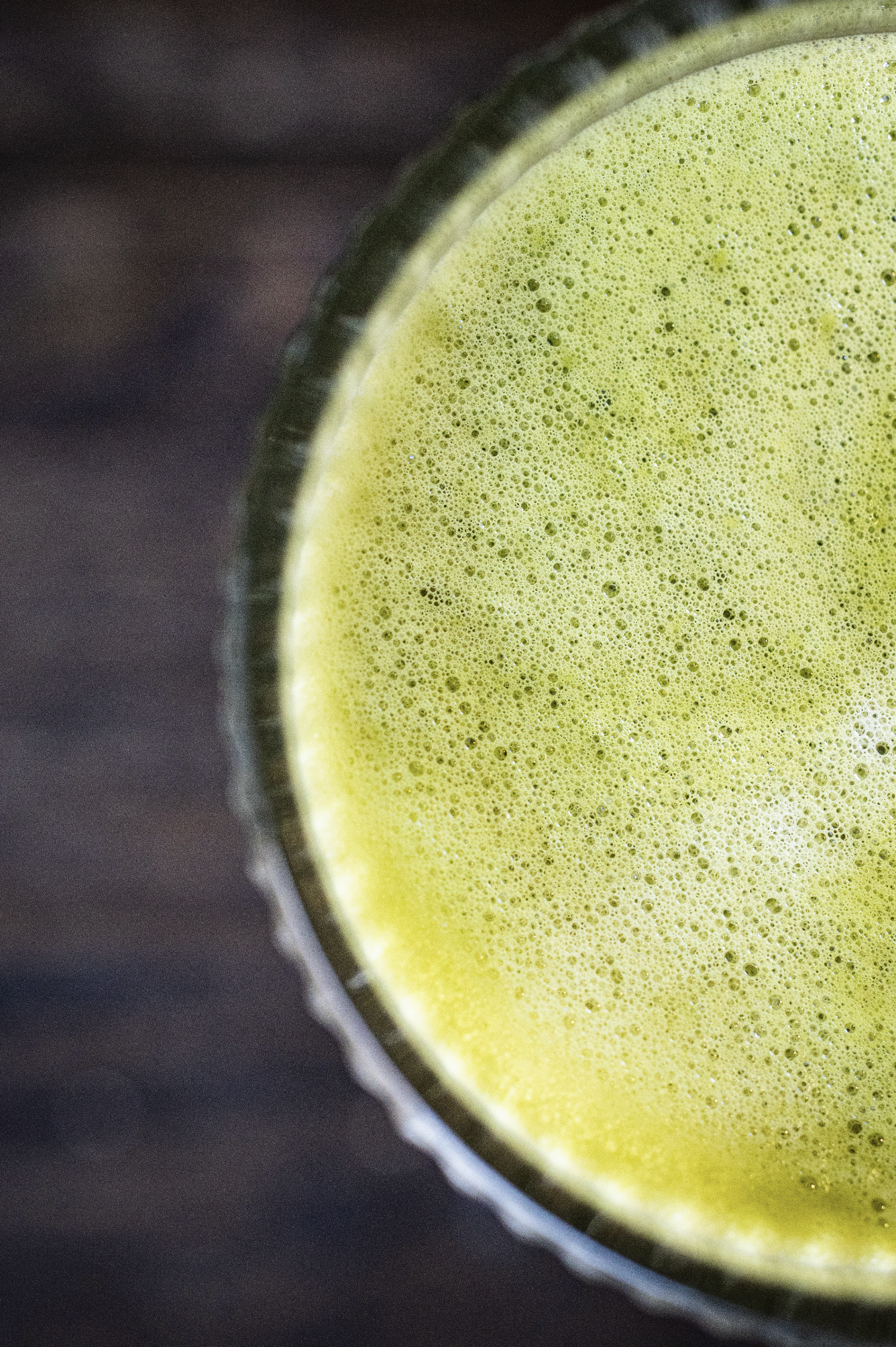 Close-up of a glass of green juice or smoothie with a frothy surface on a dark wooden surface
