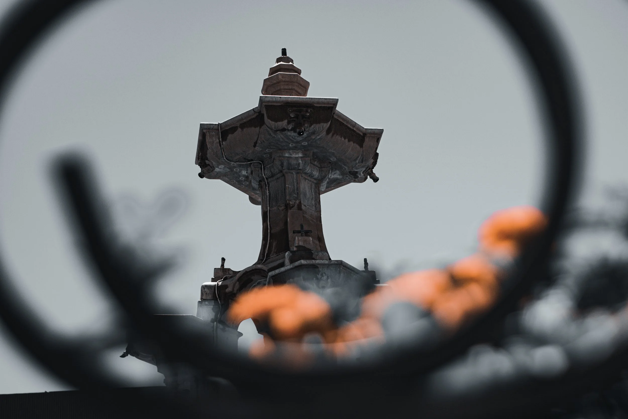 View of a church steeple seen through a circular opening with blurred orange flowers in the foreground.