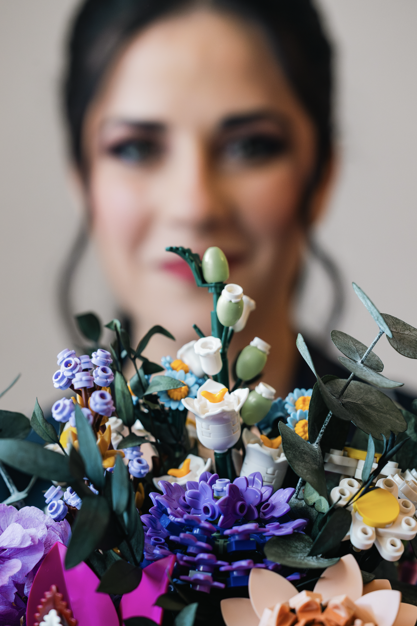 Blurred woman in background holding a colorful LEGO flower bouquet.