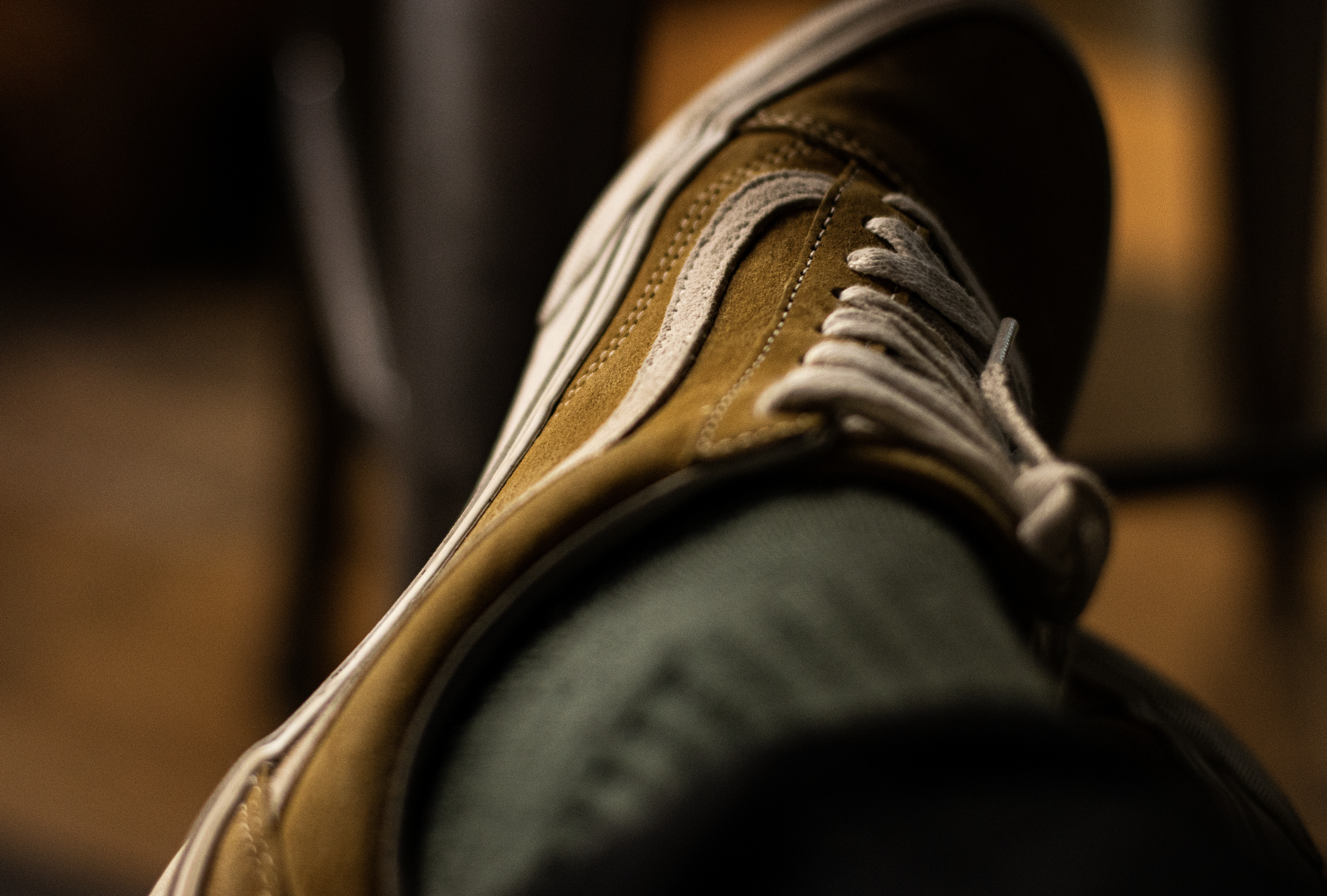 Close-up of a brown and beige sneaker with white laces on a person's foot, blurred background.