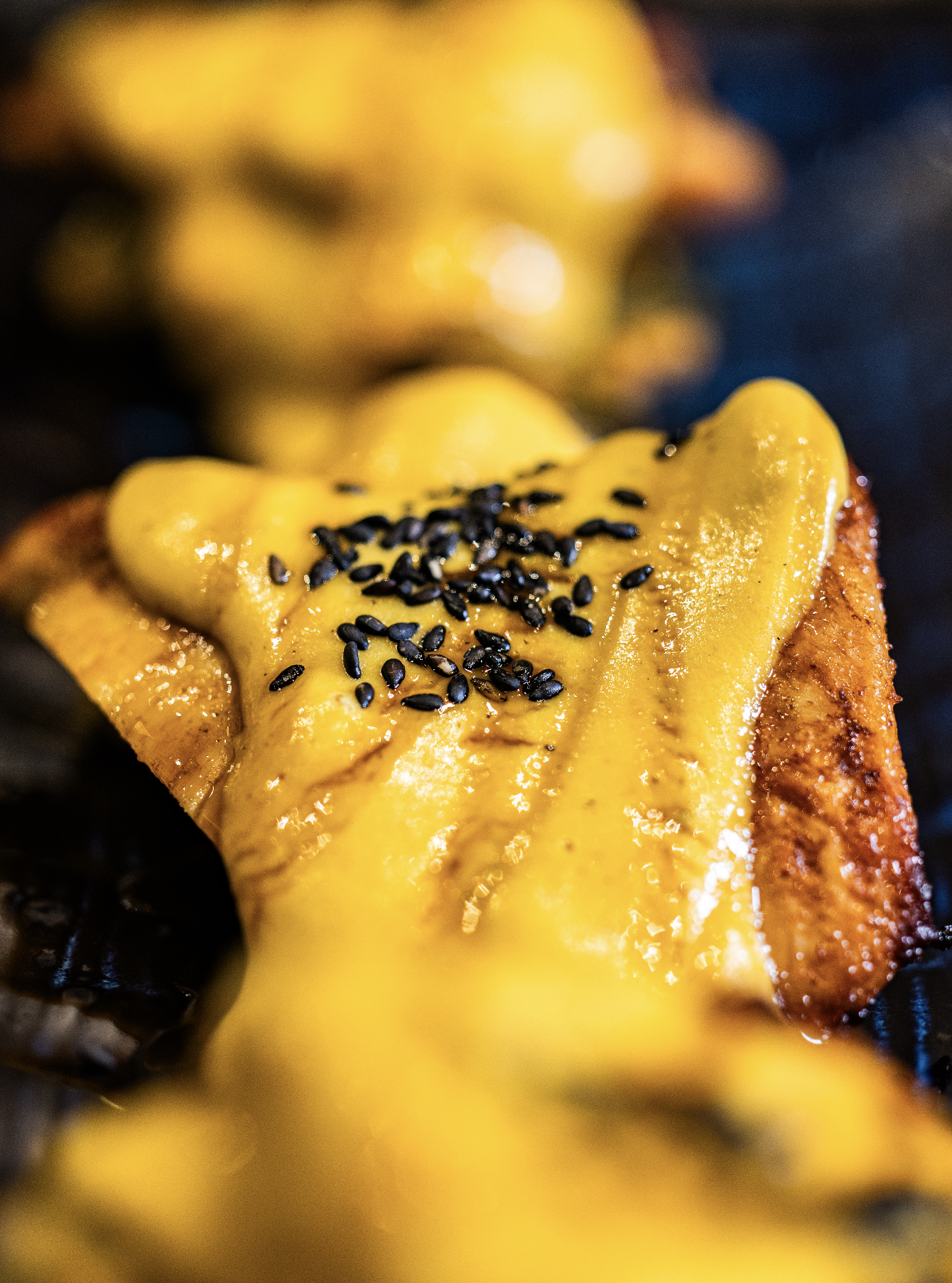 Close-up of a burger with melted yellow cheese and black sesame seeds on top, on a grill.
