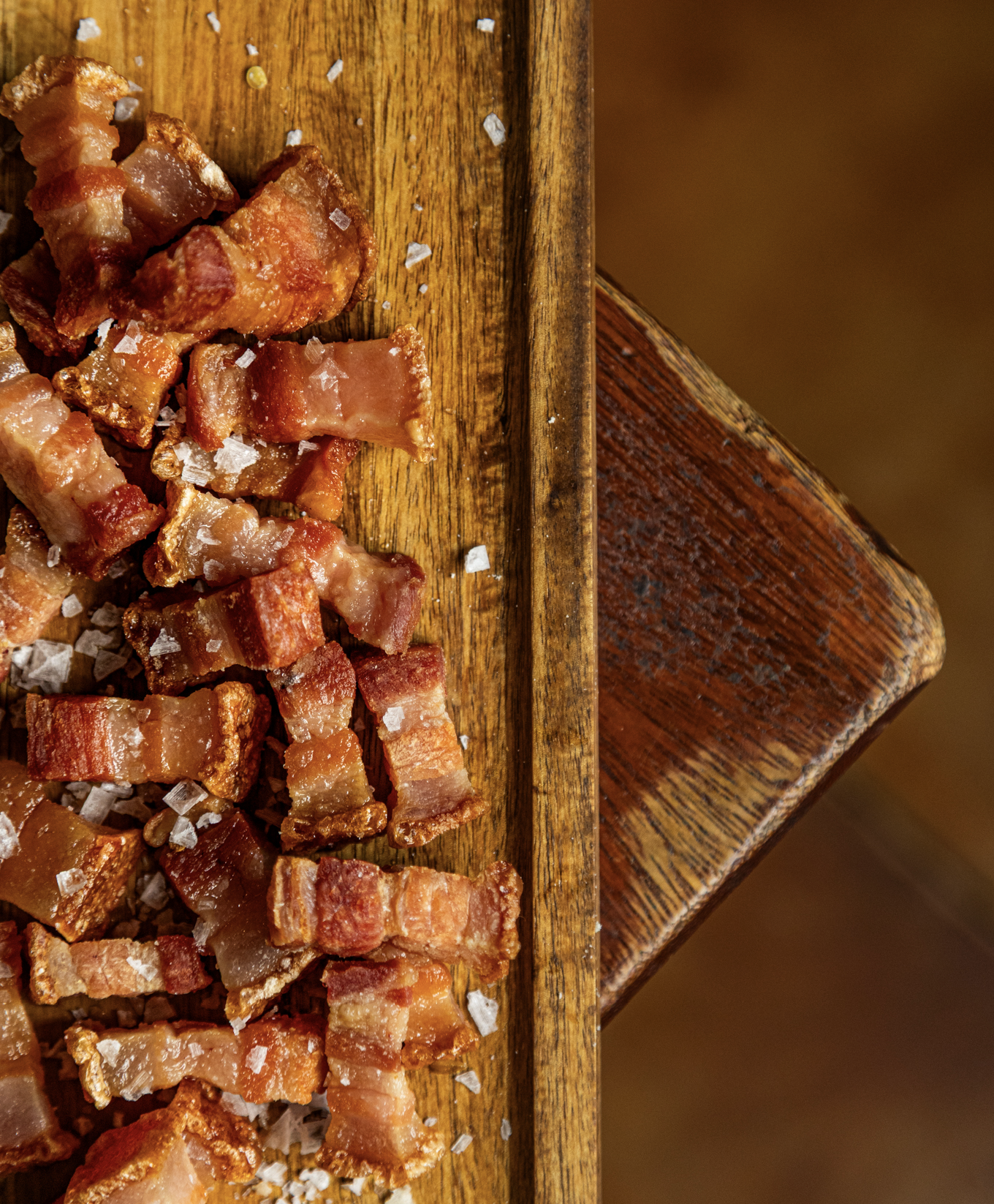 Crispy cooked bacon slices topped with coarse sea salt on a wooden cutting board.
