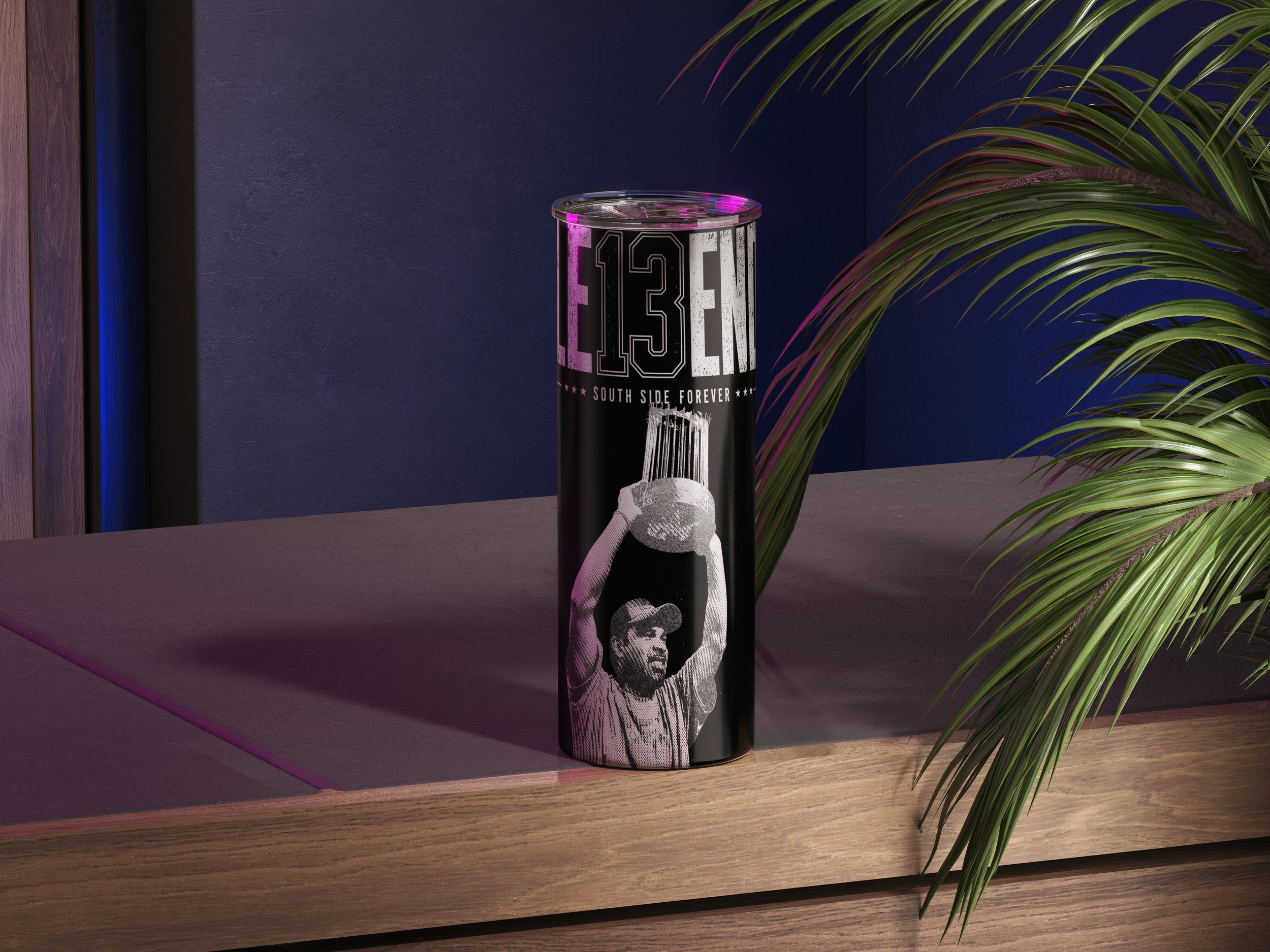 A cylindrical tumbler with black and white graphics featuring a person and text reading "13th South Side Forever". The tumbler is placed on a wooden surface with a dark wall and leafy green plant in the background.