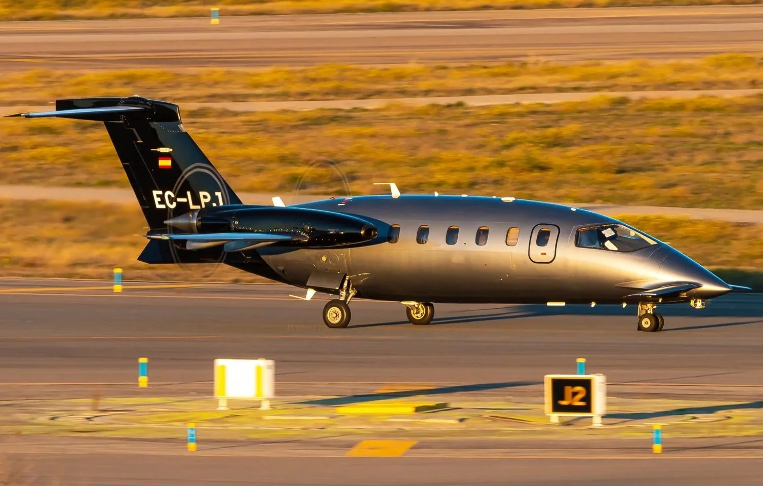 A sleek, black private jet taxiing on a runway during sunset with a clear sky and desert landscape in the background.