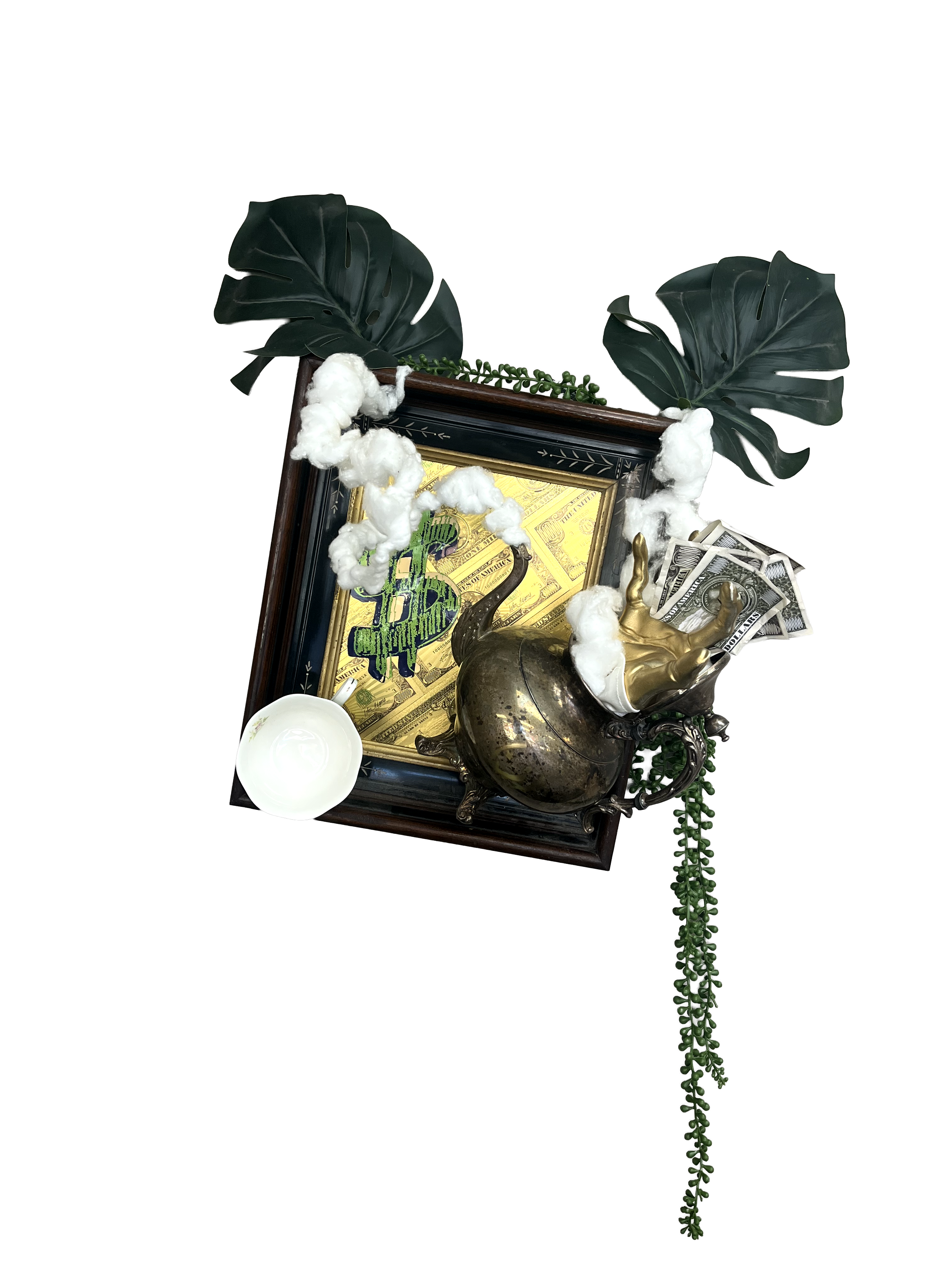 Arrangement including large dark green leaves, cotton-like decorative elements, a framed picture of a dollar sign, silver and gold decorative objects, a small white bowl, and dollar bills, with a green leafy sprig, on a black background.