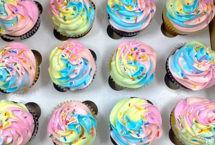 Colorful cupcakes with pink, blue, yellow, and green frosting topped with rainbow sprinkles.