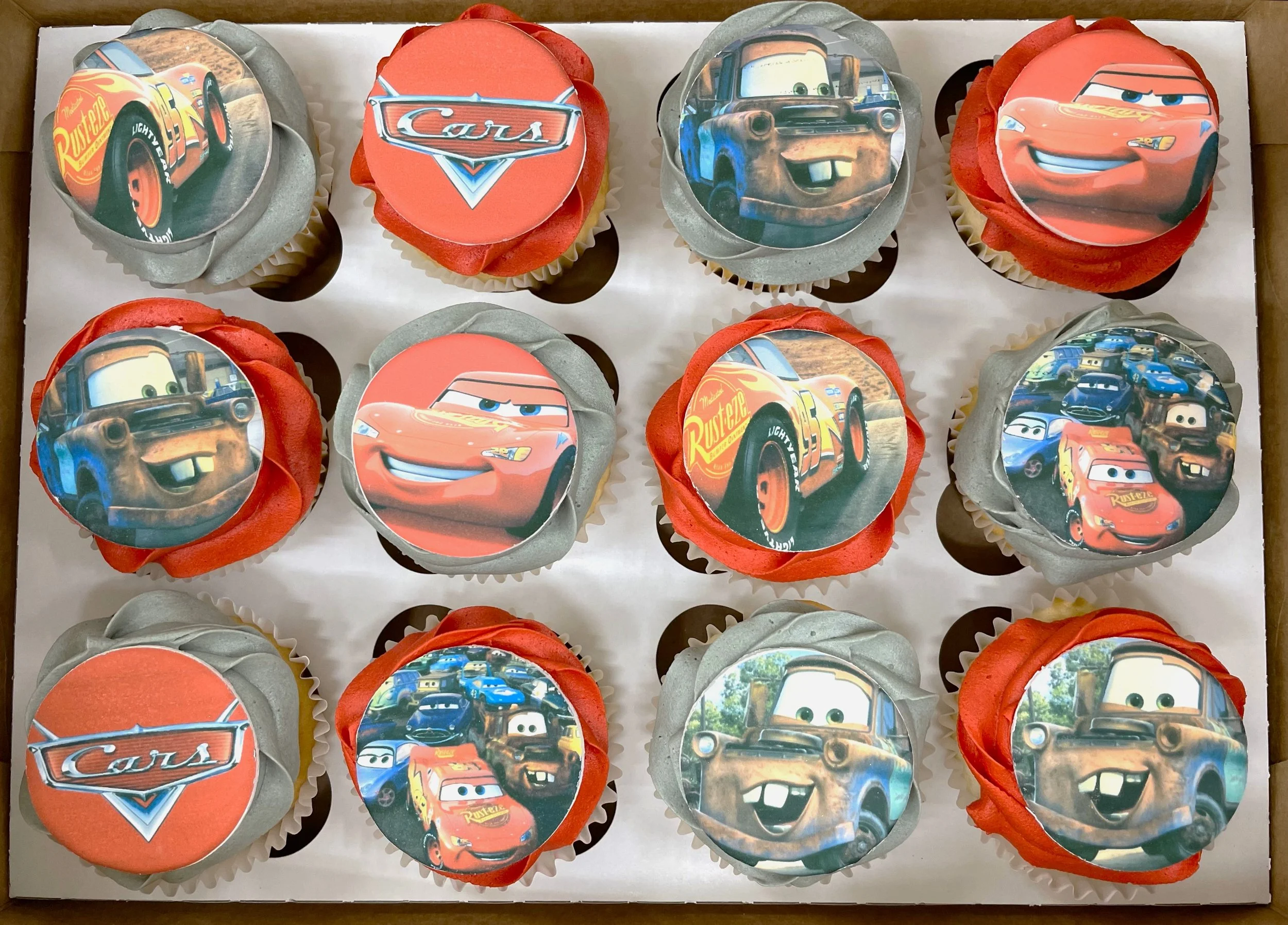 Cupcakes decorated with images of characters and scenes from the animated movie 'Cars', including Lightning McQueen and Mater.