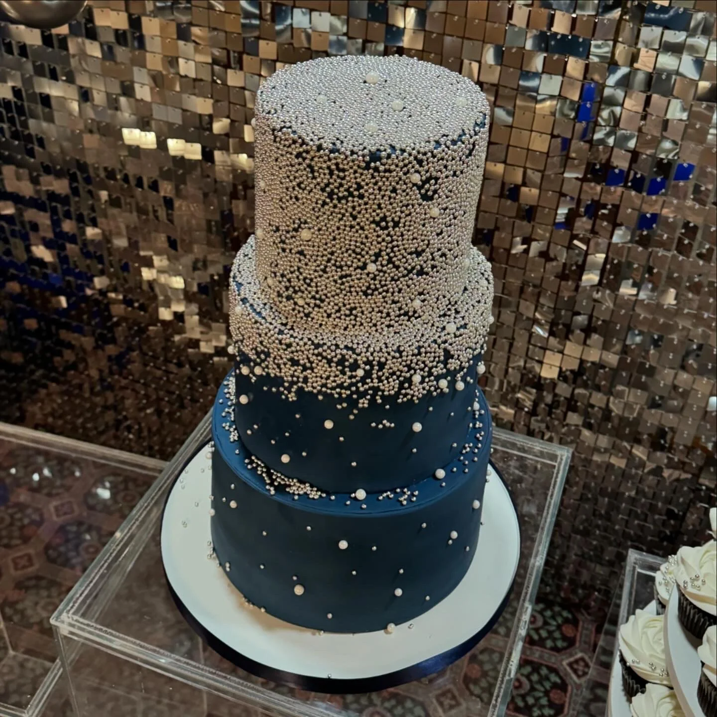 A four-tier navy blue wedding cake decorated with white edible pearls and sugar beads.