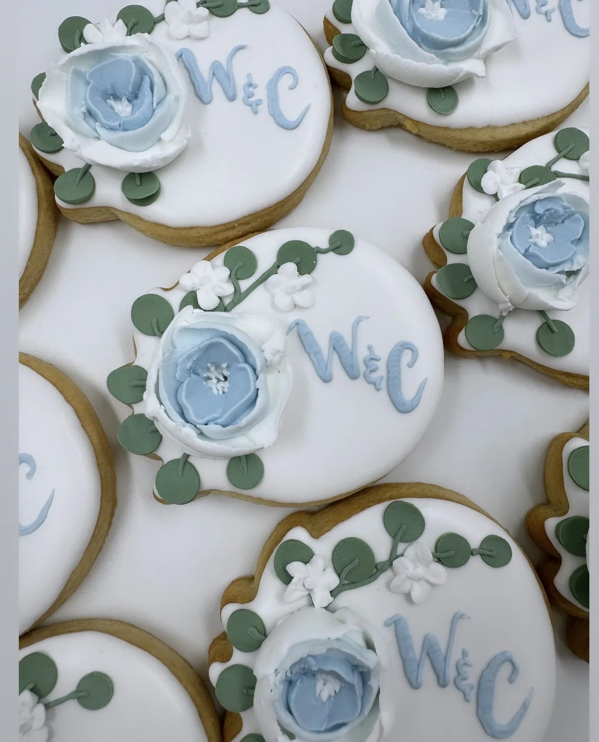 Decorated cookies with white icing, blue roses, green leaves.