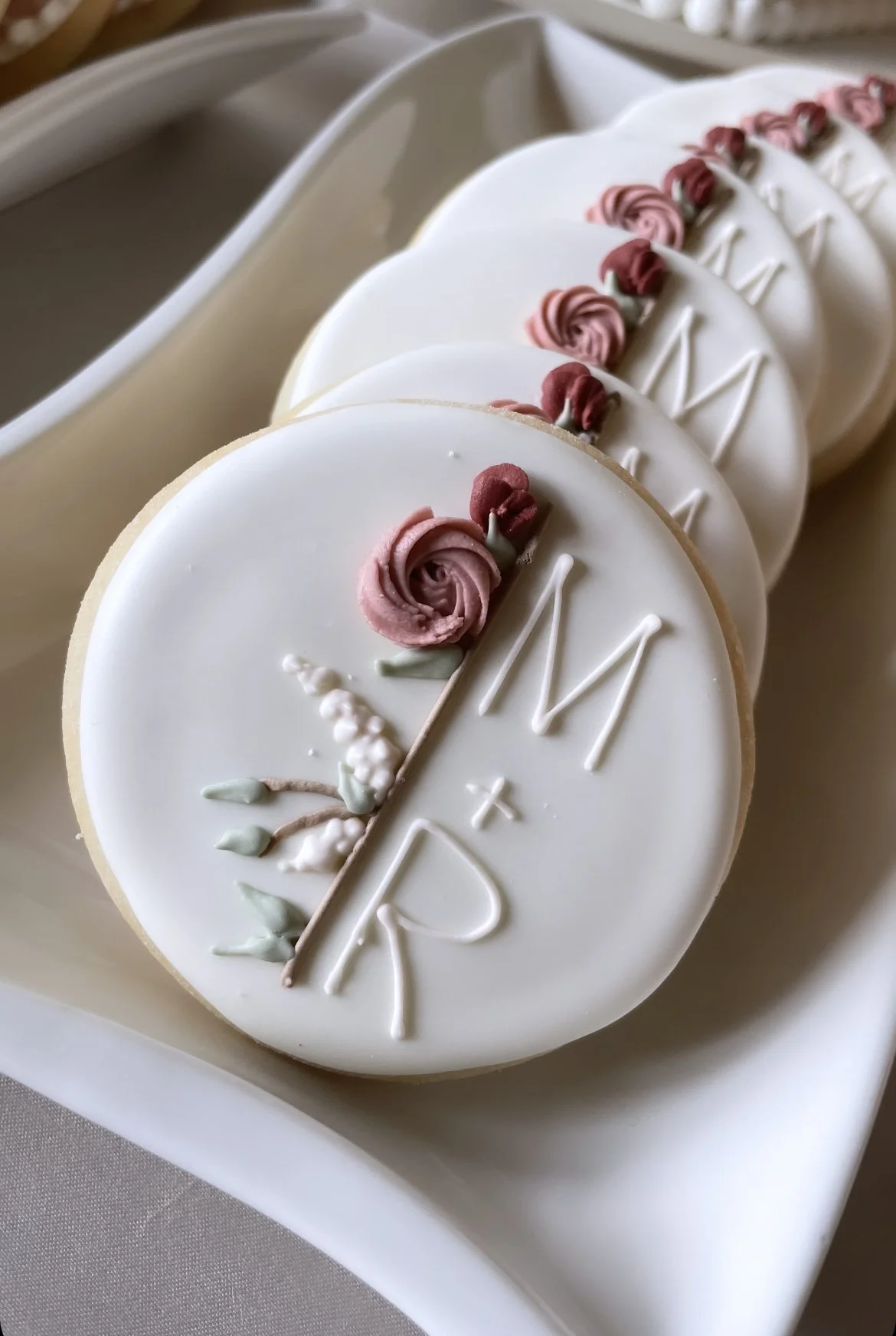 Decorated cookies with white glaze, pink and red buttercream roses, and the words 'M + R' written in white icing.