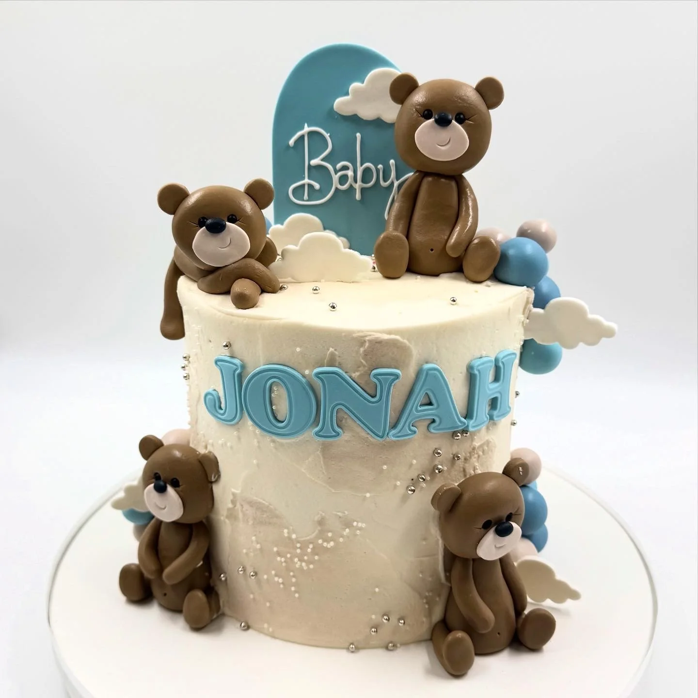 A decorated birthday cake with teddy bears, clouds, and blue and white accents.