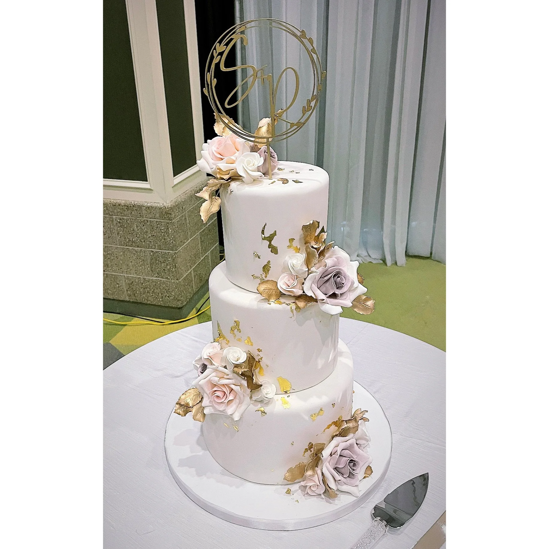 Three-tiered white wedding cake decorated with pink and lavender sugar roses, gold leaf accents.