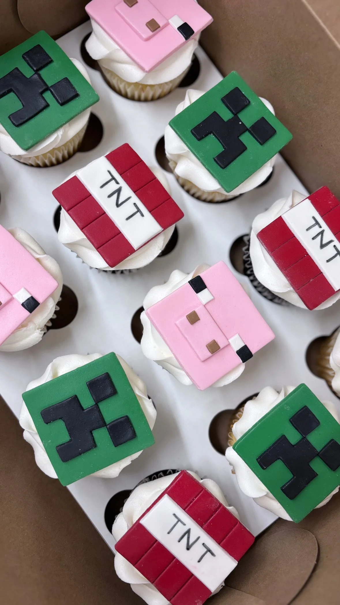Cupcakes decorated with pixelated Minecraft-themed toppers, including green, pink, and red blocks with designs resembling Creeper faces and TNT.