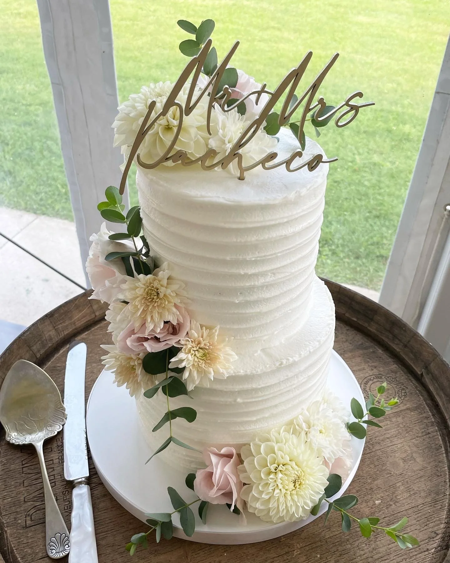 A two-tier white wedding cake decorated with white and blush pink flowers and greenery.