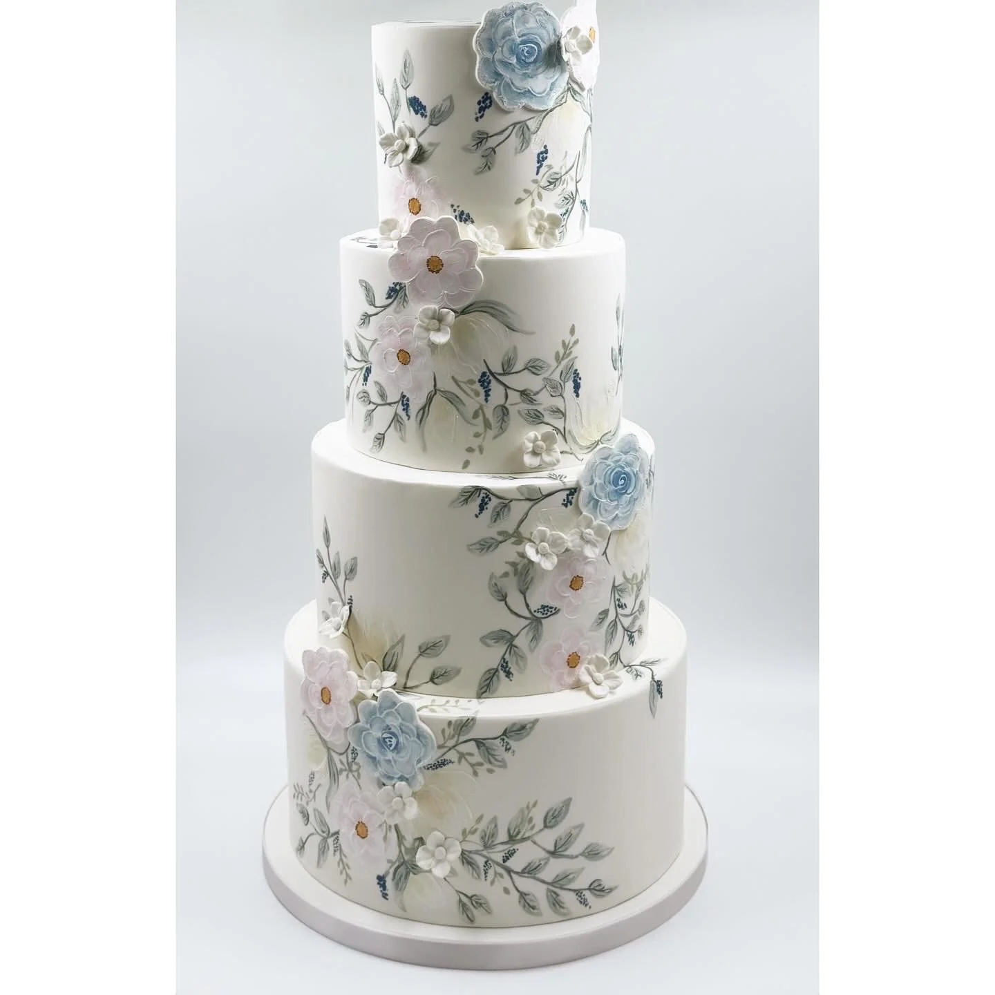 Four-tier white wedding cake decorated with pastel-colored flower and leaf patterns.