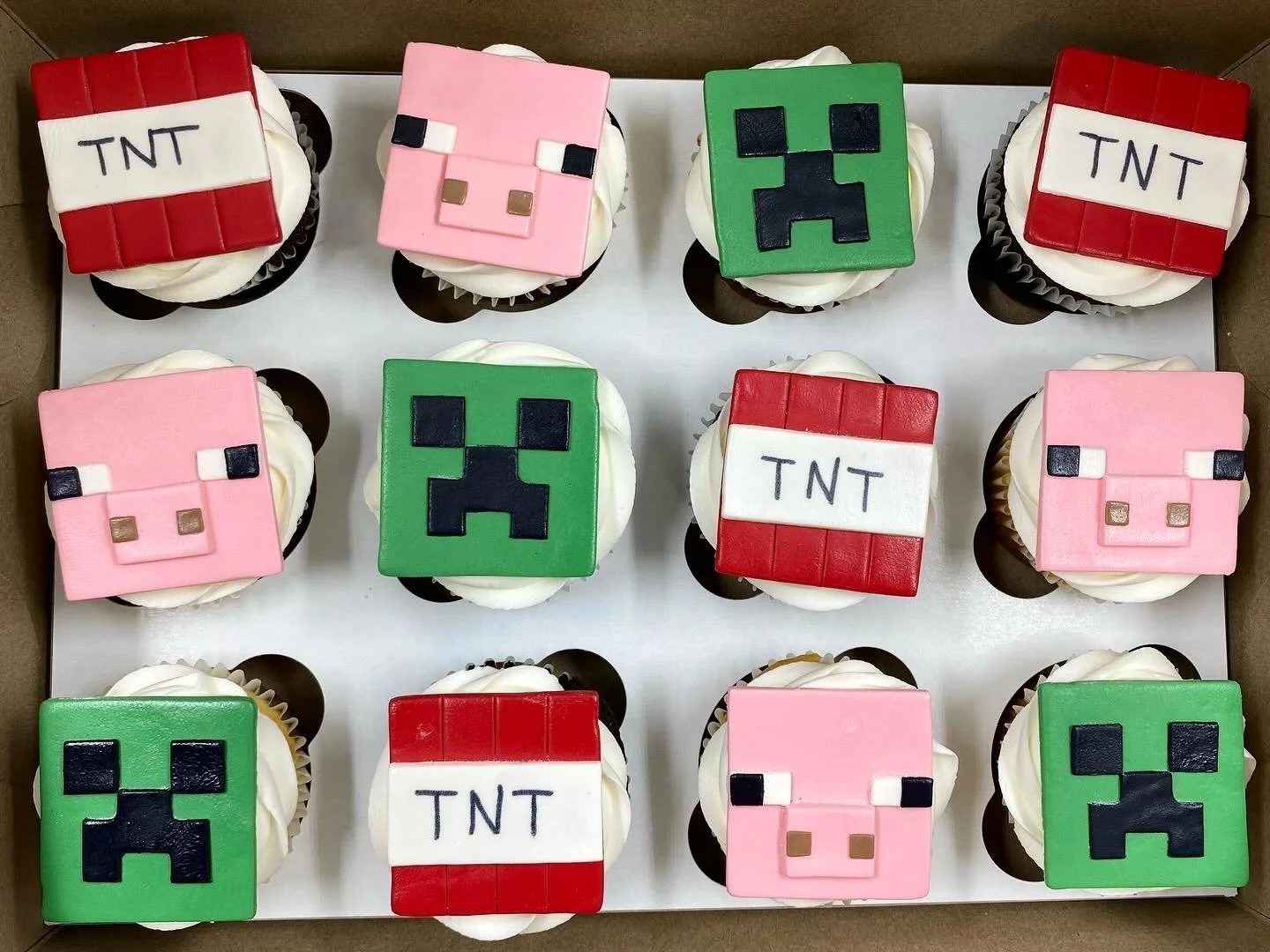 Decorative cupcakes themed after Minecraft characters, including Creeper and pig, and TNT blocks, topped with colorful fondant decorations.