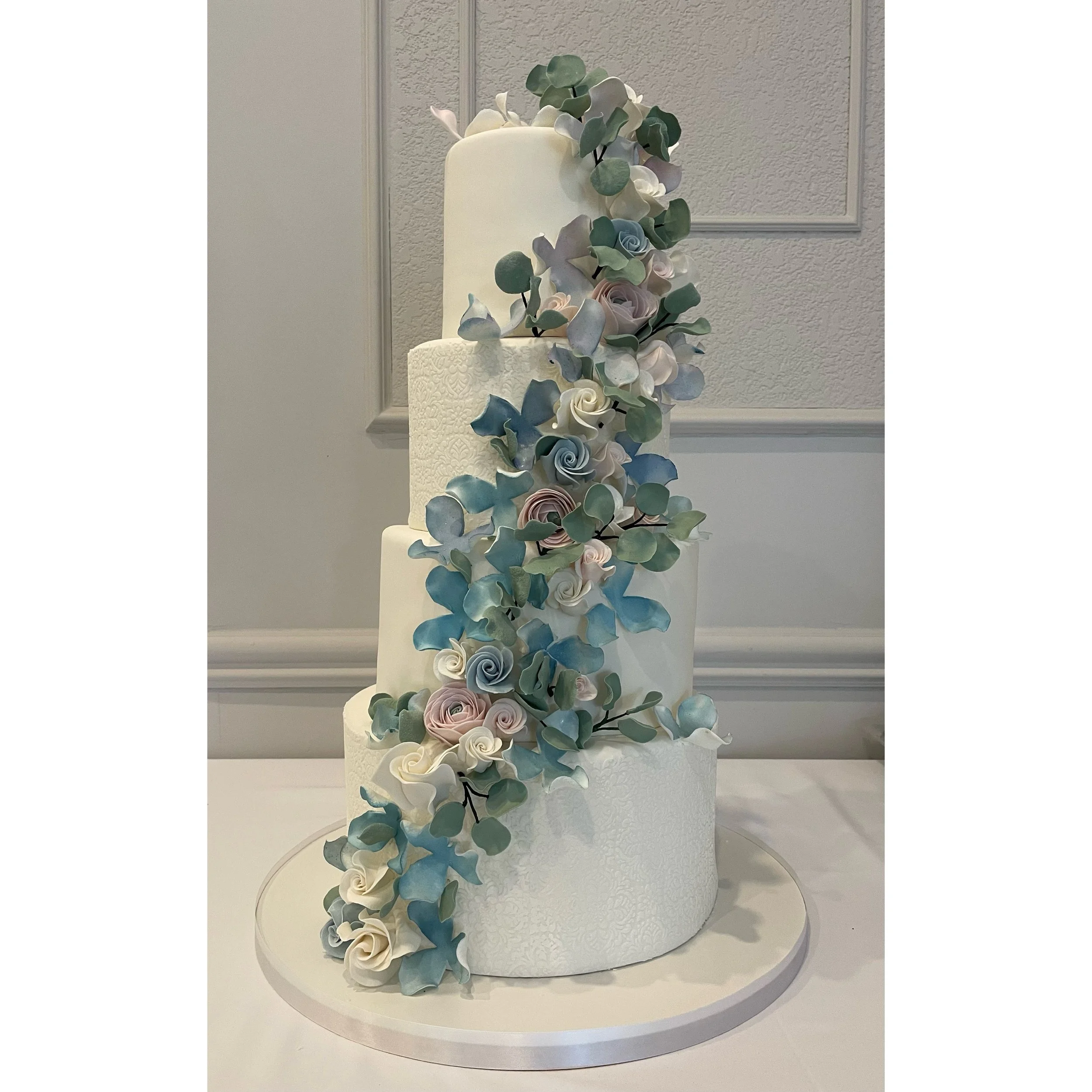 Elegant four-tier wedding cake decorated with cascading pastel-colored roses and eucalyptus leaves.